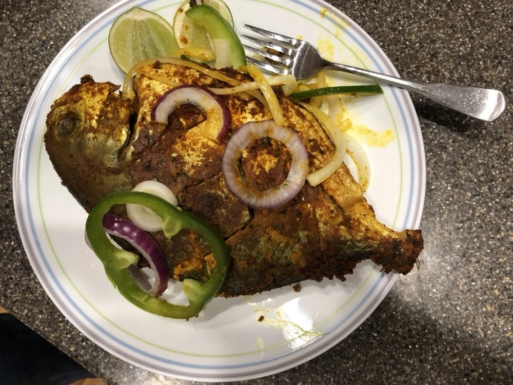 Fried fish served on a white plate with lemon and lime wedges, and sliced onions and green bell peppers