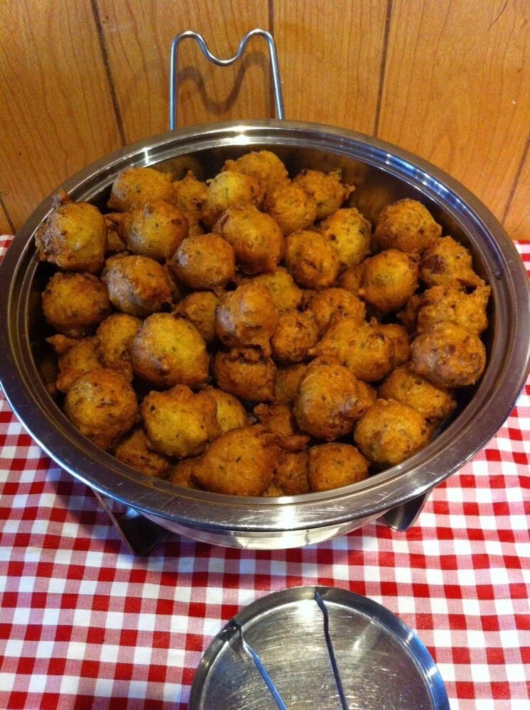 A large stainless steel bowl filled with fried dough balls, placed on a red and white checkered tablecloth