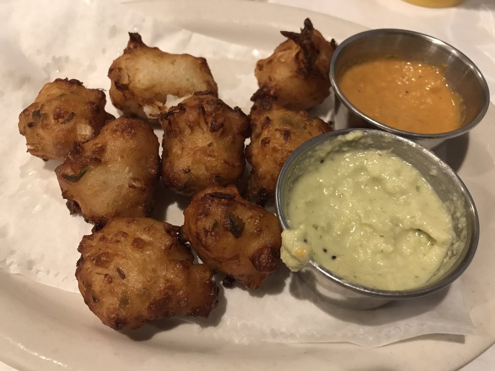 Fried food balls served with two dipping sauces in small metal cups, on a white paper-lined plate.