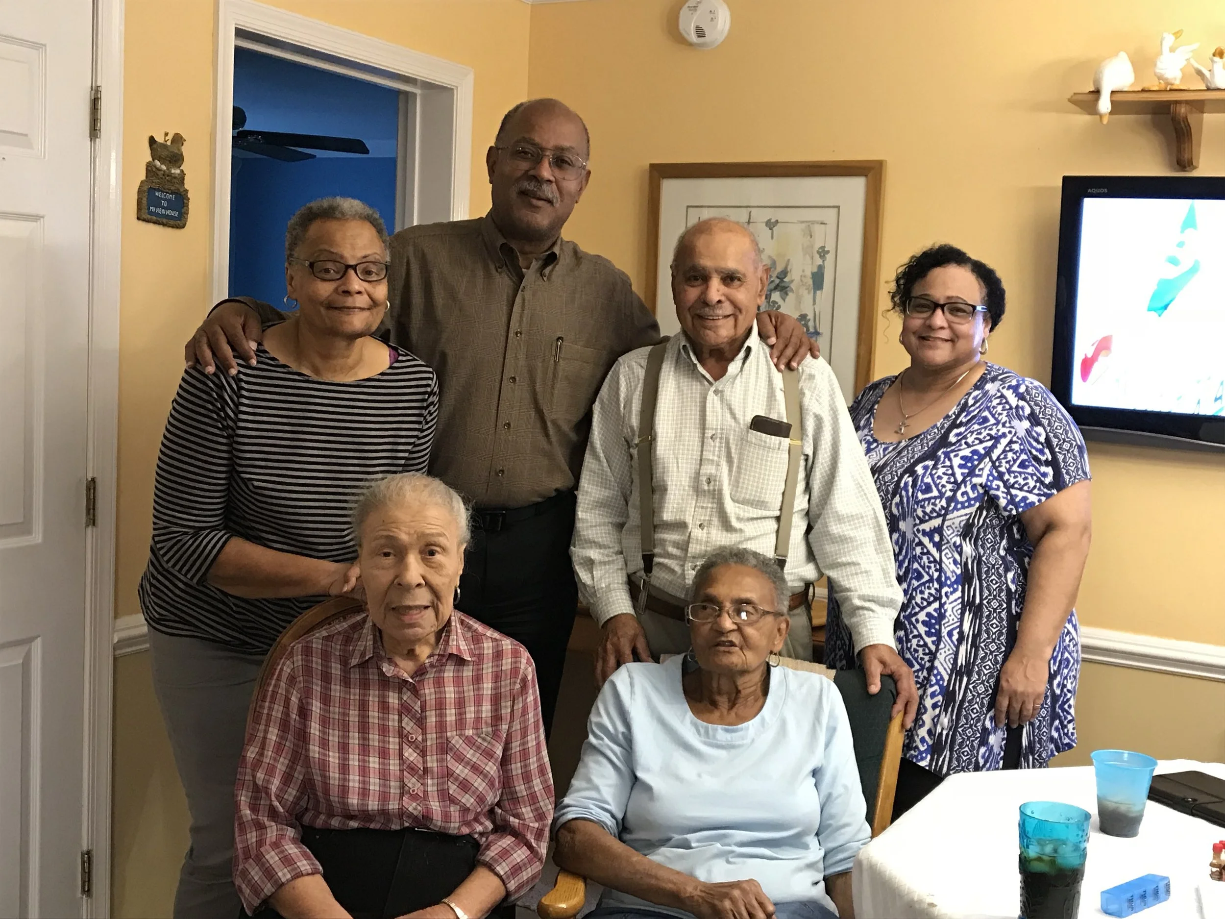 Seven older adults pose for a family photo in a living room.