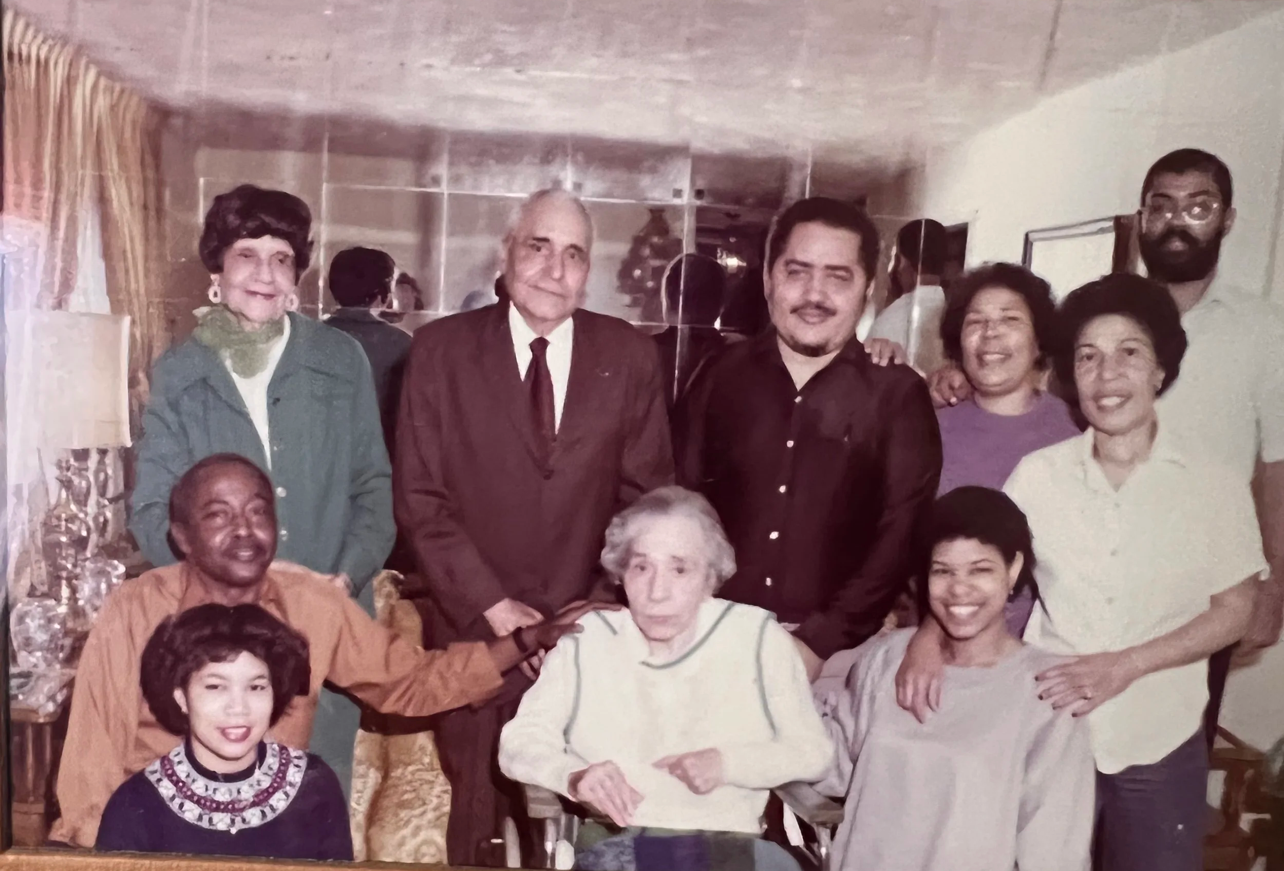 Vintage group portrait of diverse adults and children gathered indoors around an elderly woman in a wheelchair.