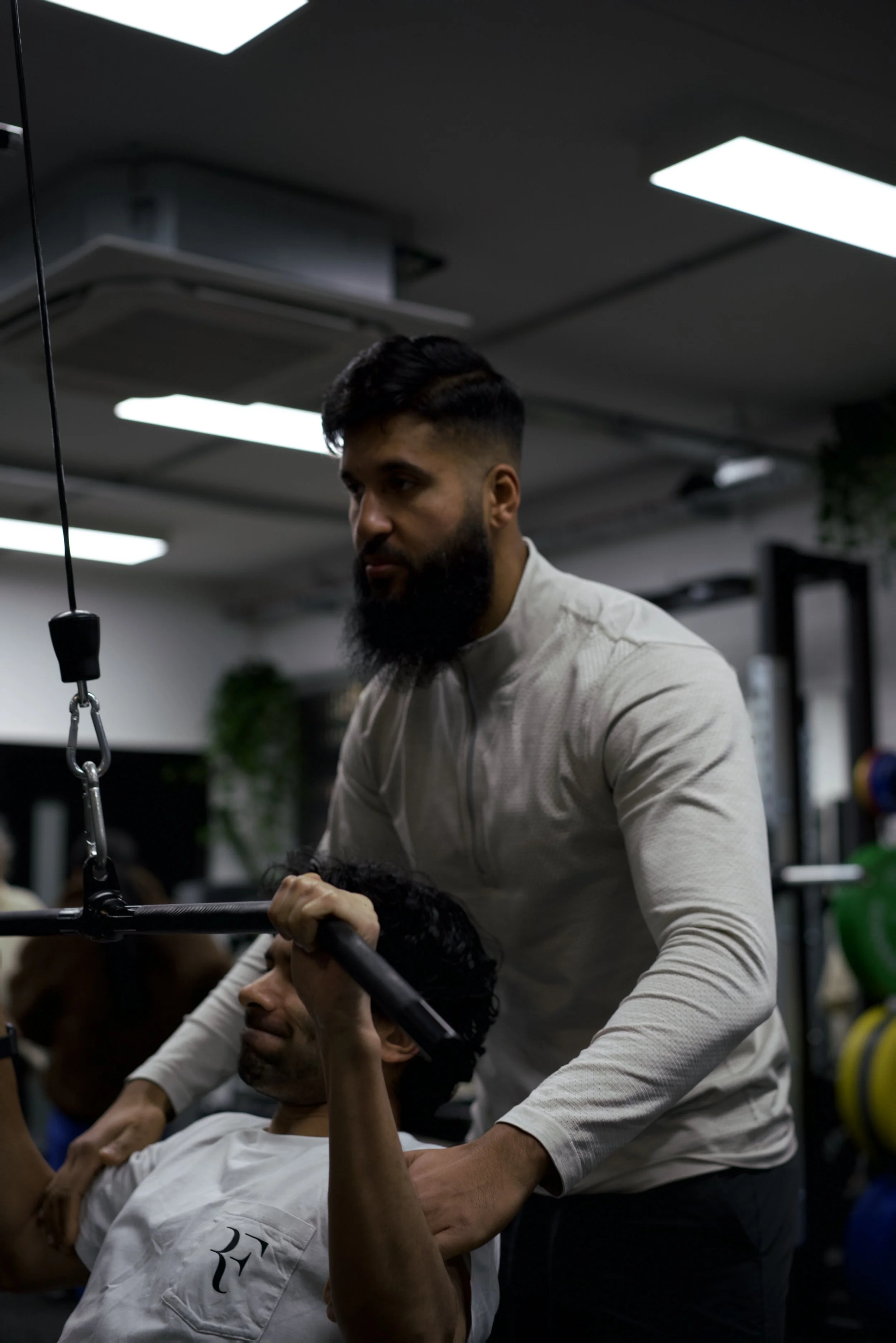 A trainer is assisting a person with a workout, providing support during an exercise in a gym setting.