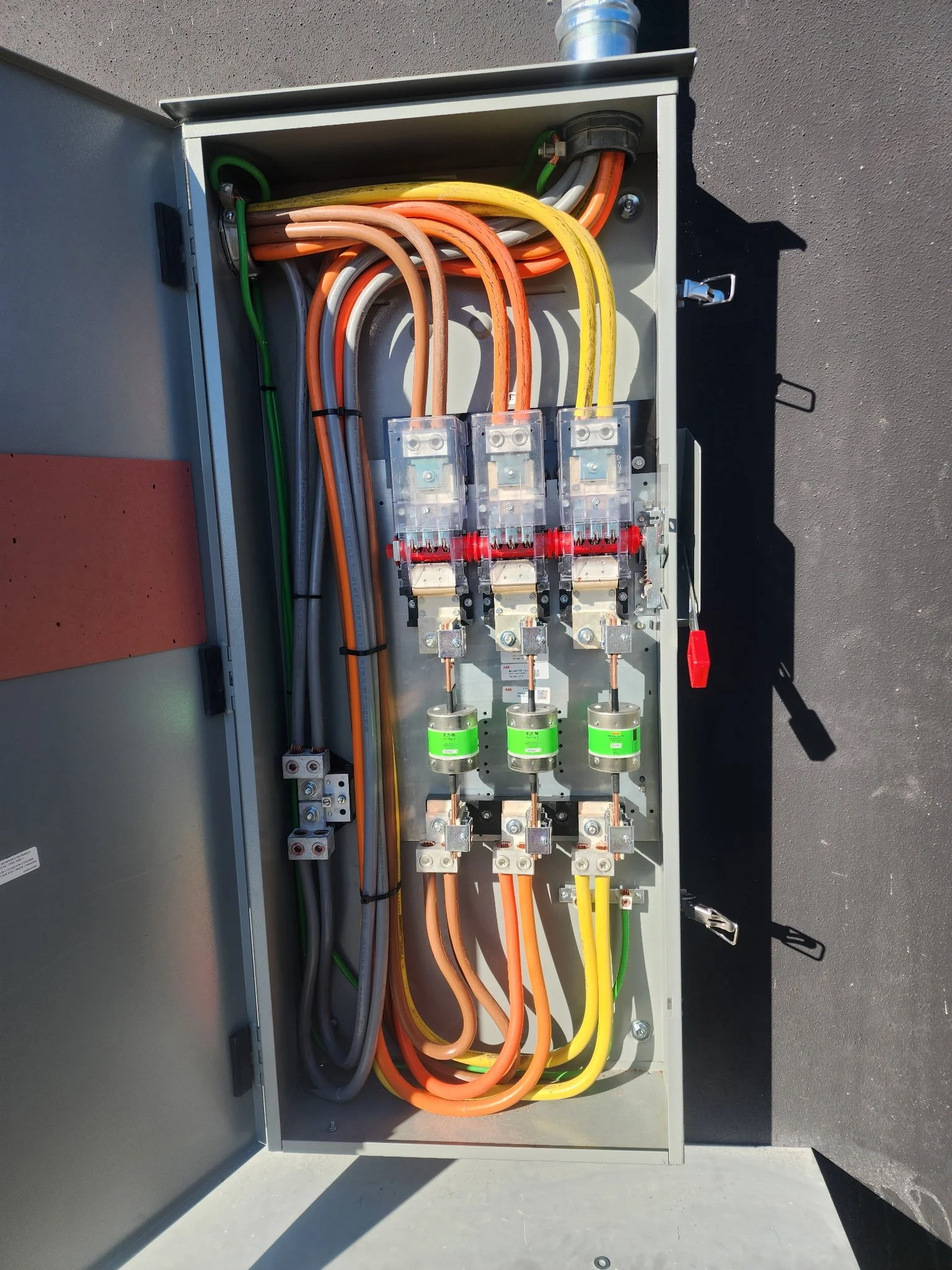Open electrical service panel with color-coded cables, three-phase fuses, and disconnect components