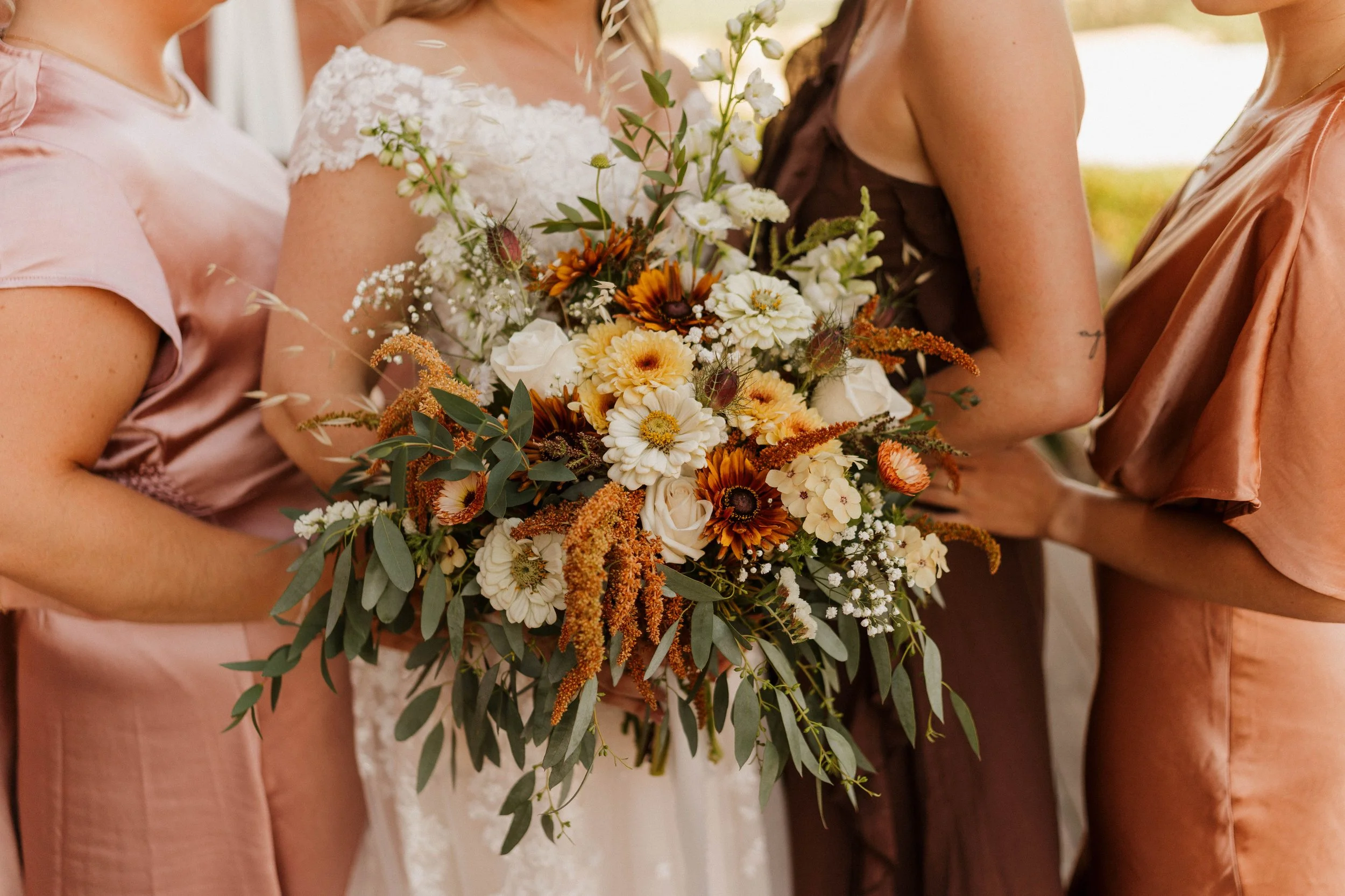 Bridal party in blush and brown dresses holding a colorful rustic wedding bouquet