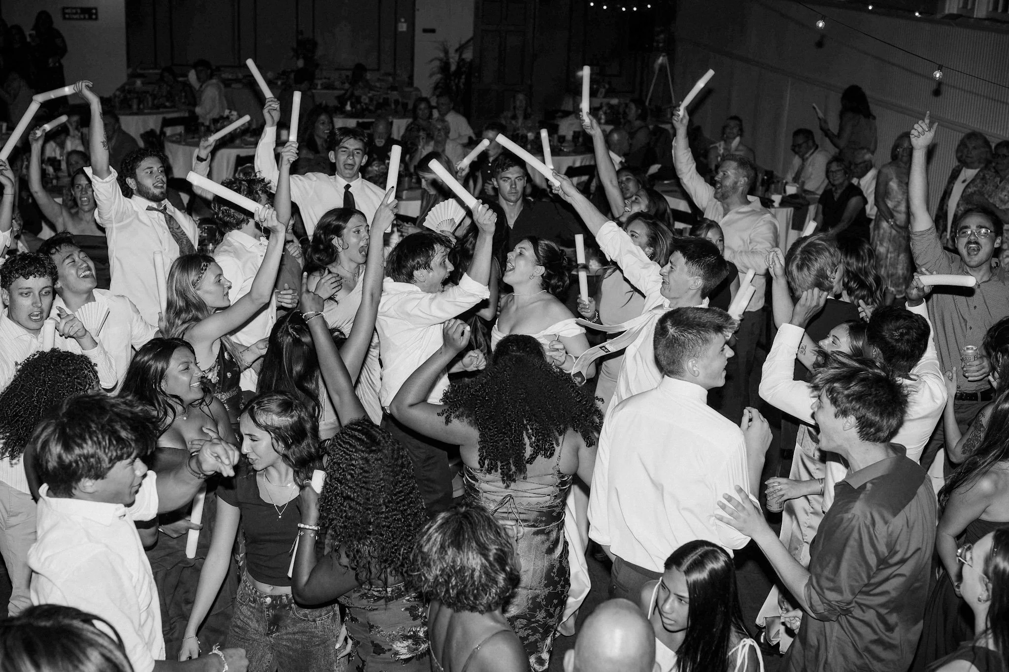 Crowd of people dancing and celebrating at a lively indoor summer wedding waving white glow sticks Labor Day weekend
