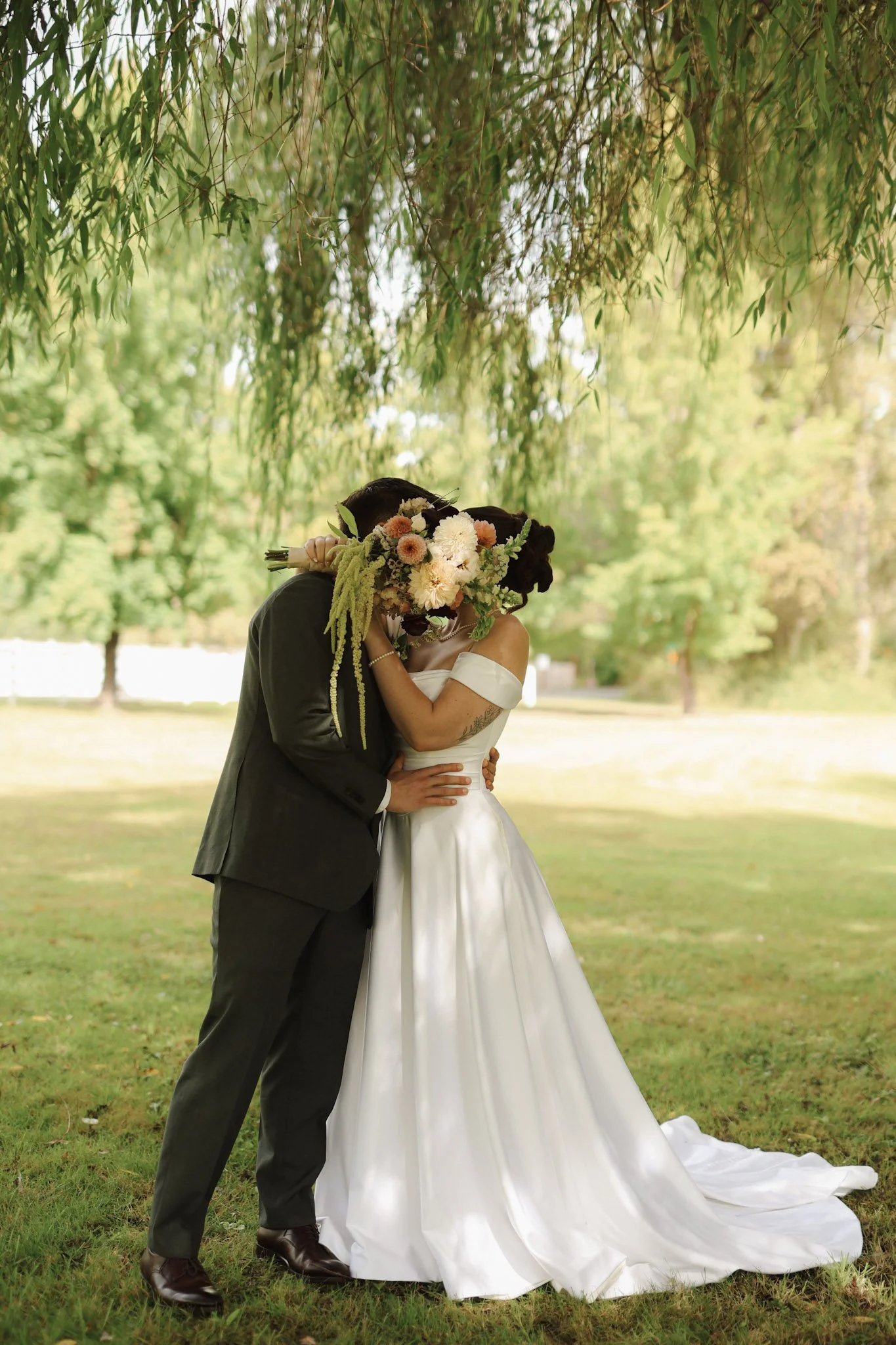 Newlywed couple embracing the Washington outdoors beneath willow trees, with the bride holding a colorful bouquet and wearing a white wedding gown.