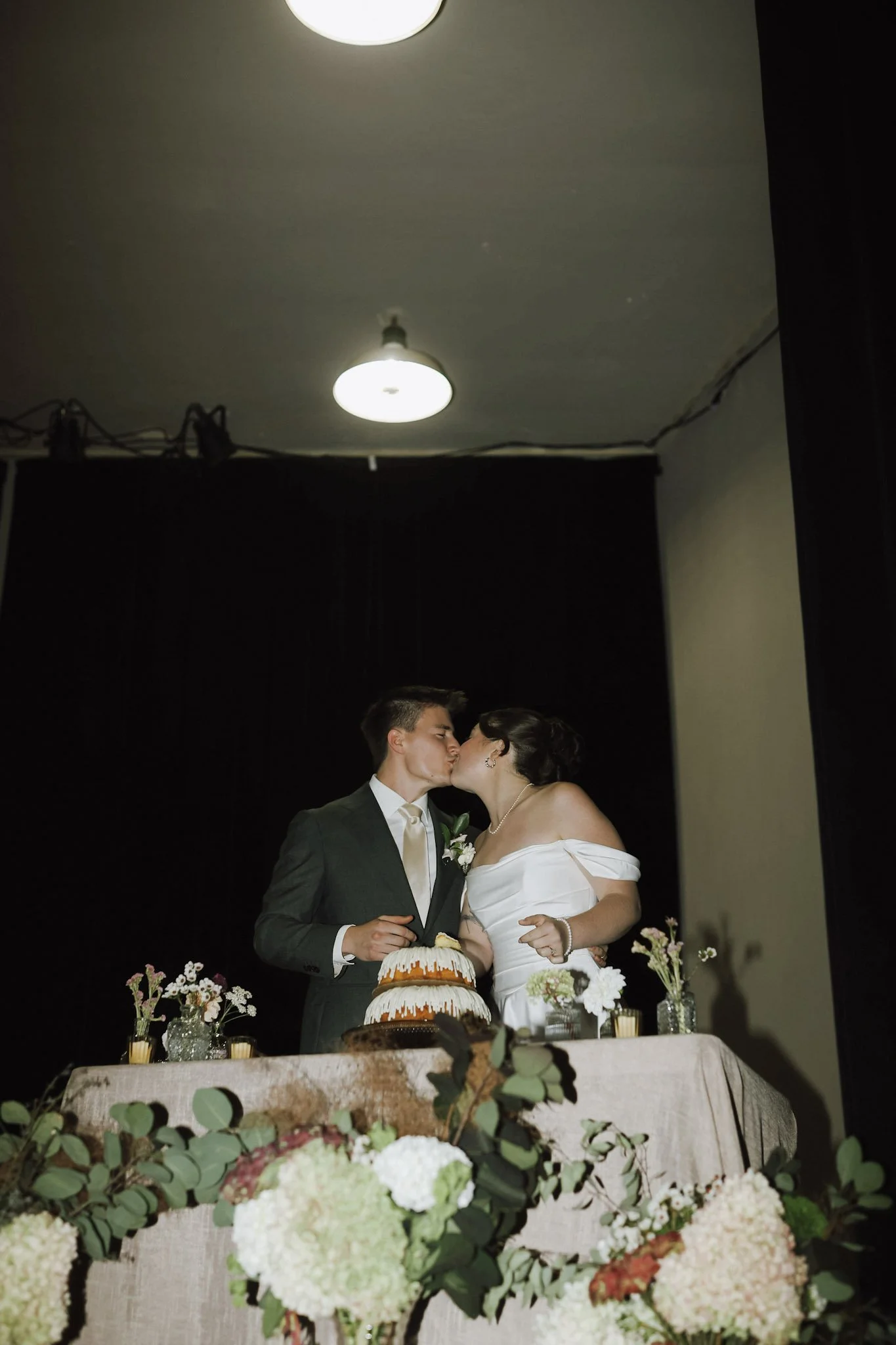Newlywed couple kissing behind a decorated wedding cake at their reception during cake cutting