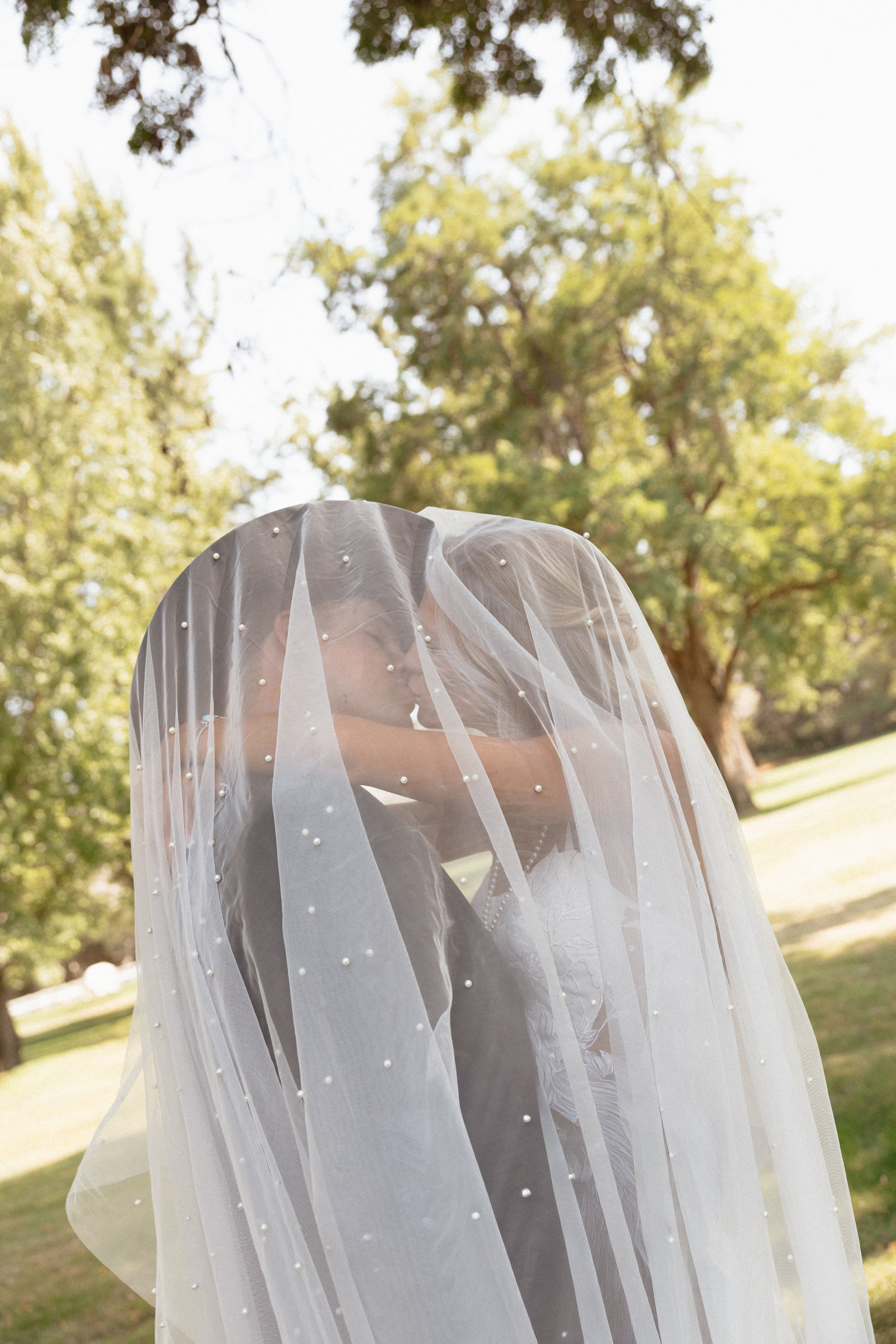 Close-up of a bride in a pearl-studded sheer veil outdoors in a sunlit garden