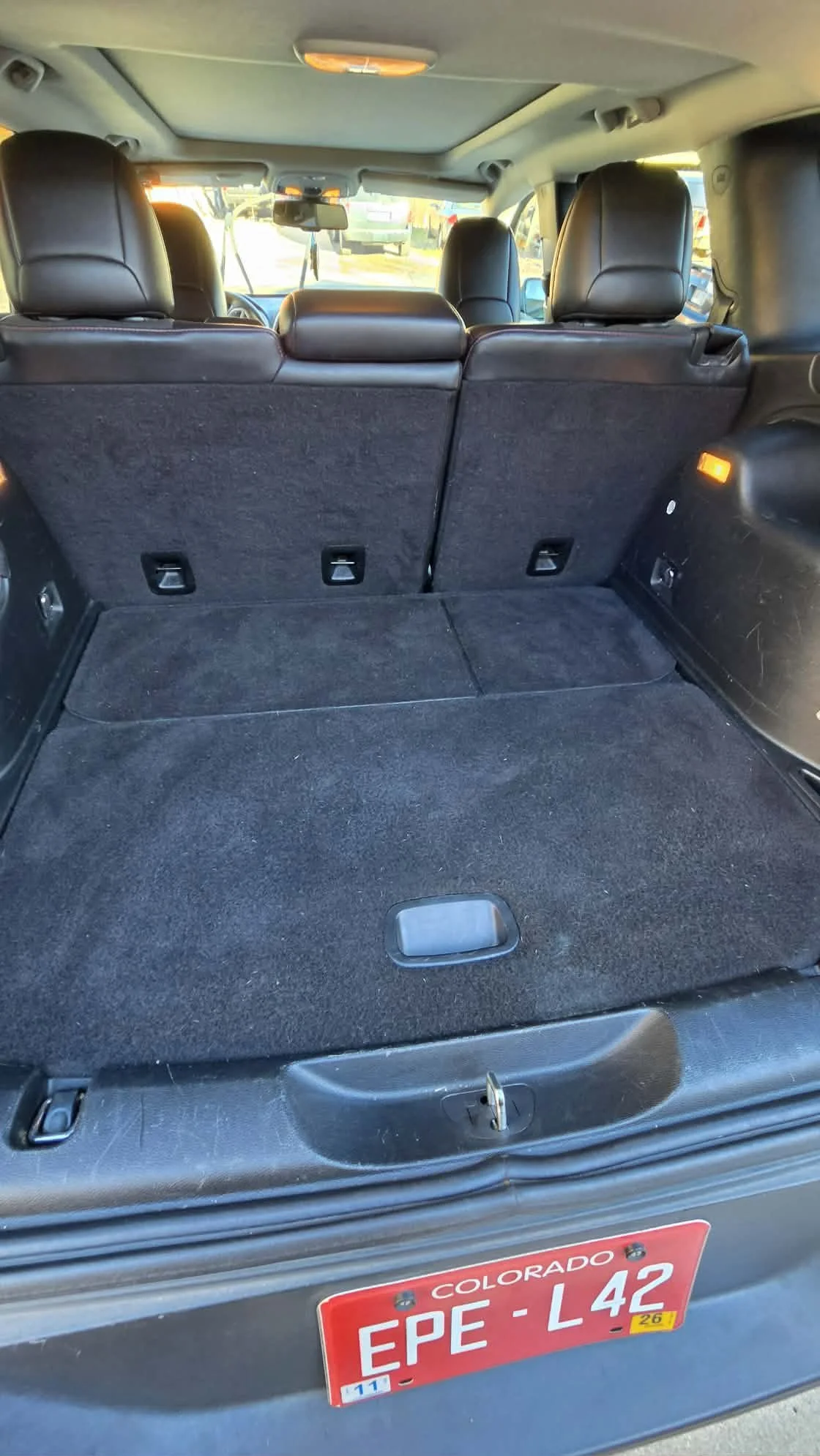 Open SUV cargo area with folded rear seats, black carpeting, and a red Colorado license plate.