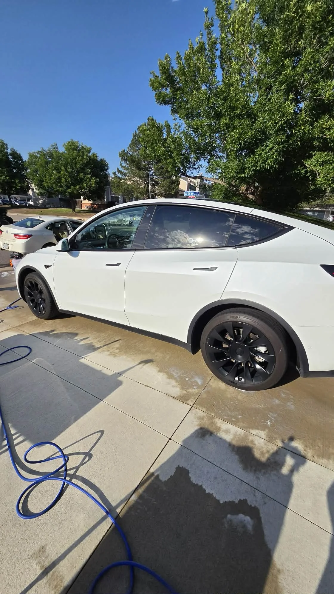 White Tesla electric car being washed on a residential driveway with a blue hose.