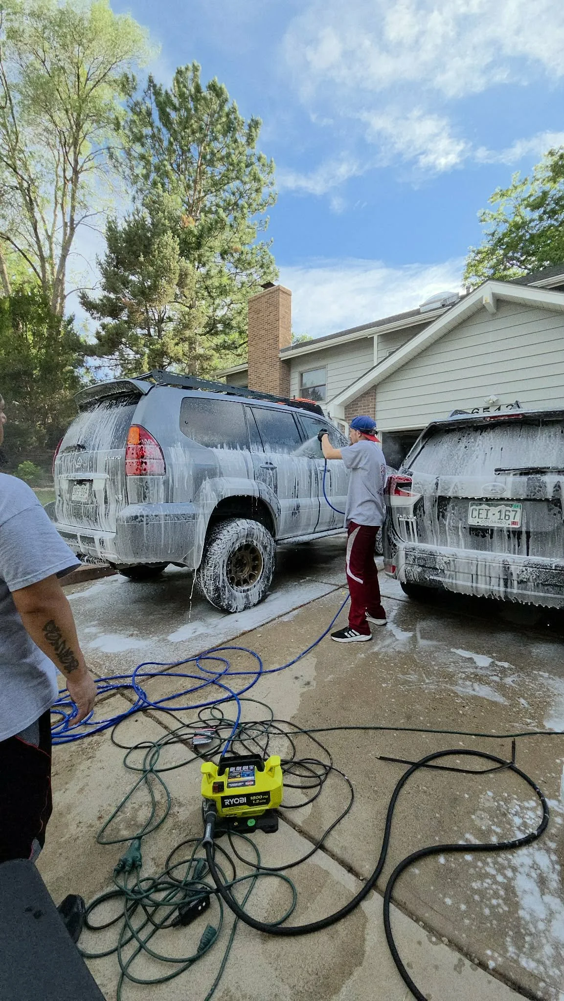 Person pressure-washing a soapy SUV and minivan in a residential driveway