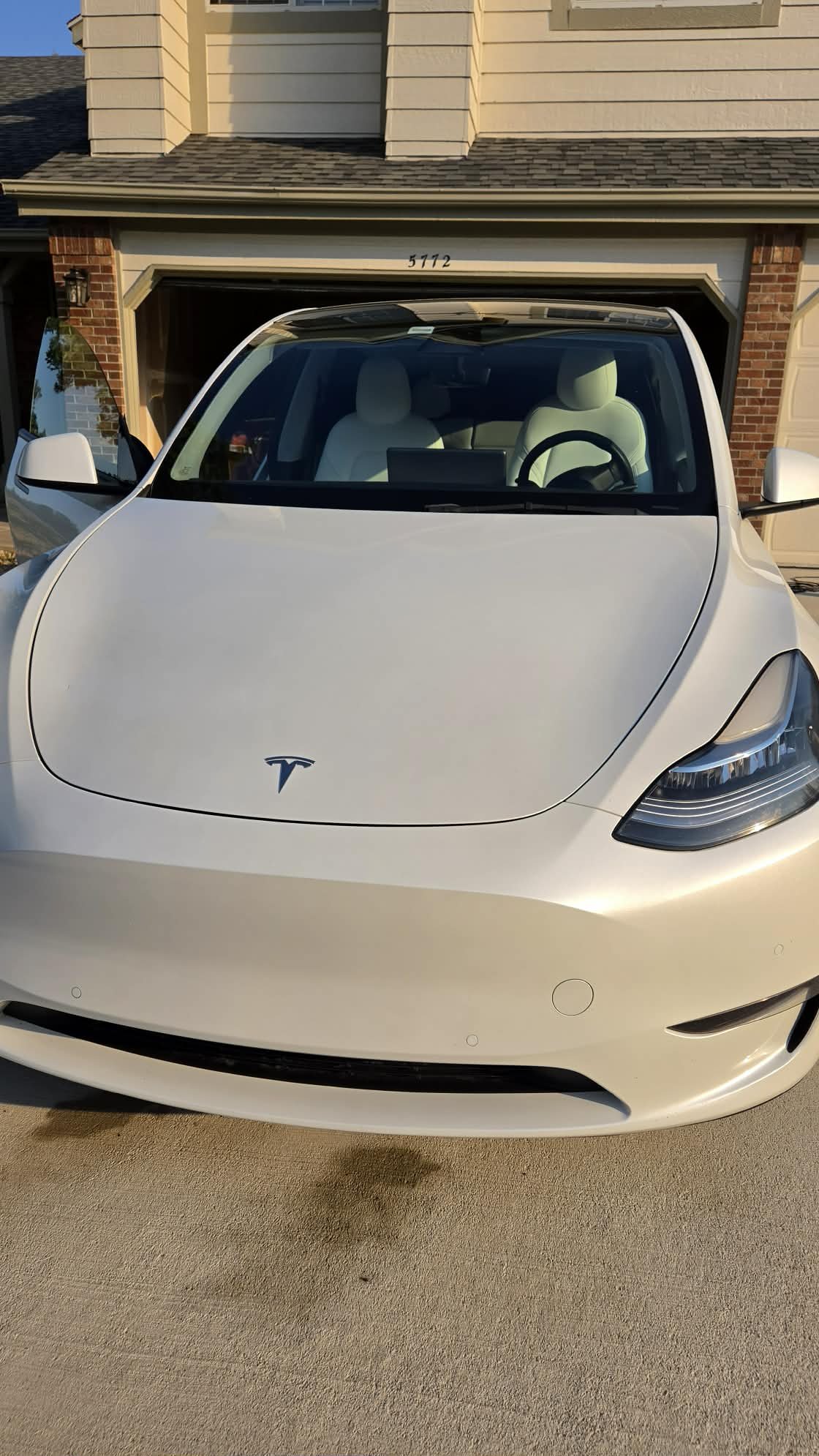 Front view of a white Tesla parked in a residential driveway in front of a garage.