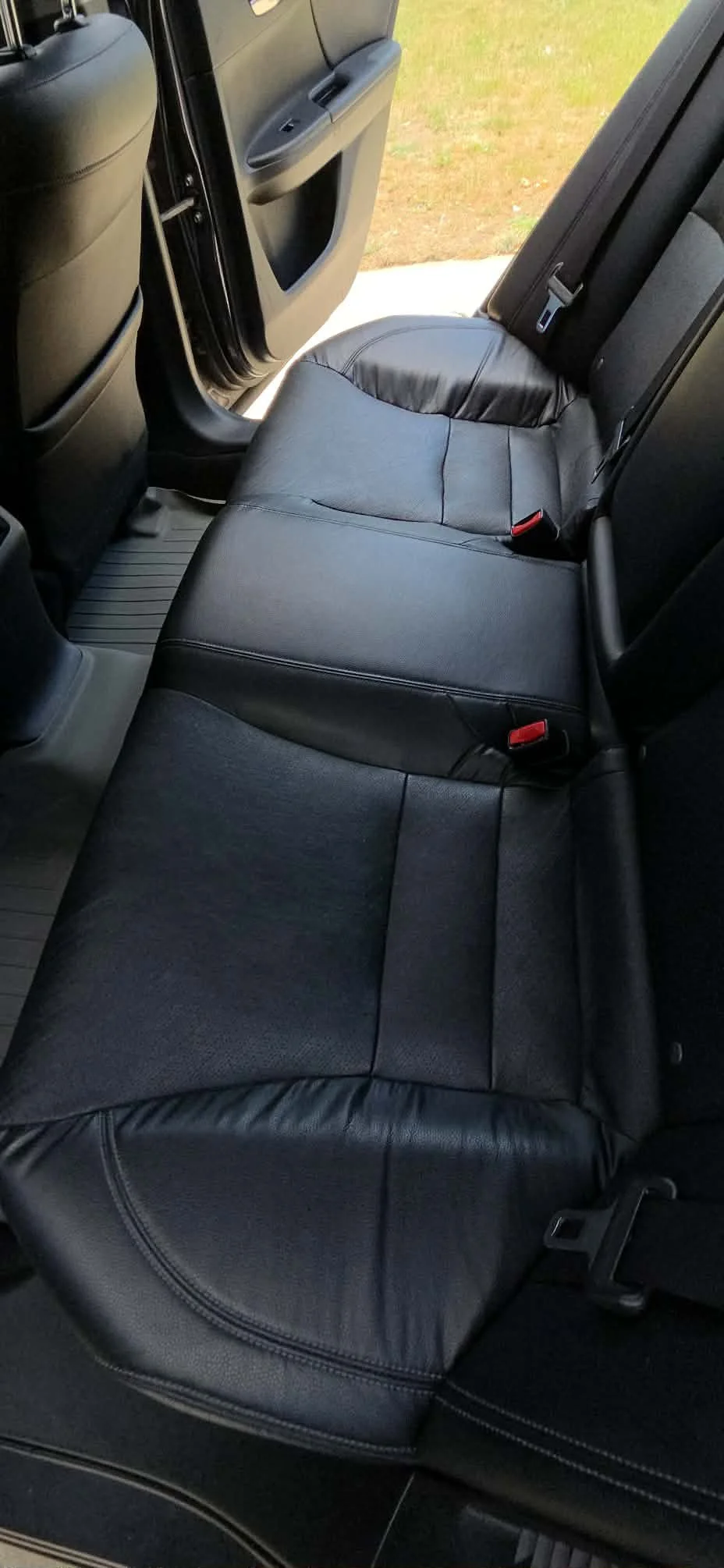 Black leather rear seats and floor mats inside a vehicle with the rear door open