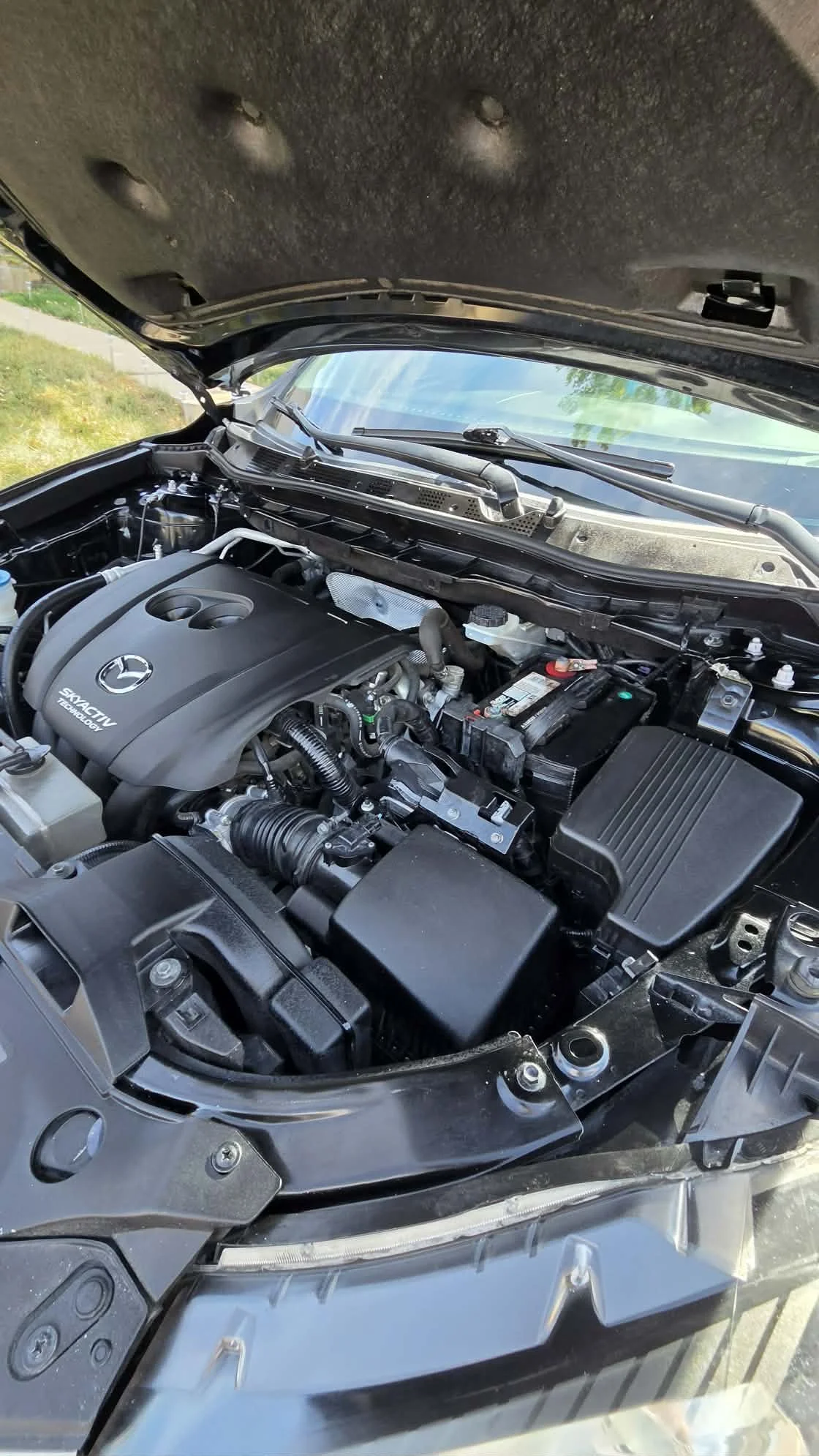 Open Mazda hood showing the Skyactiv Technology engine, battery, air intake, and other engine bay components.