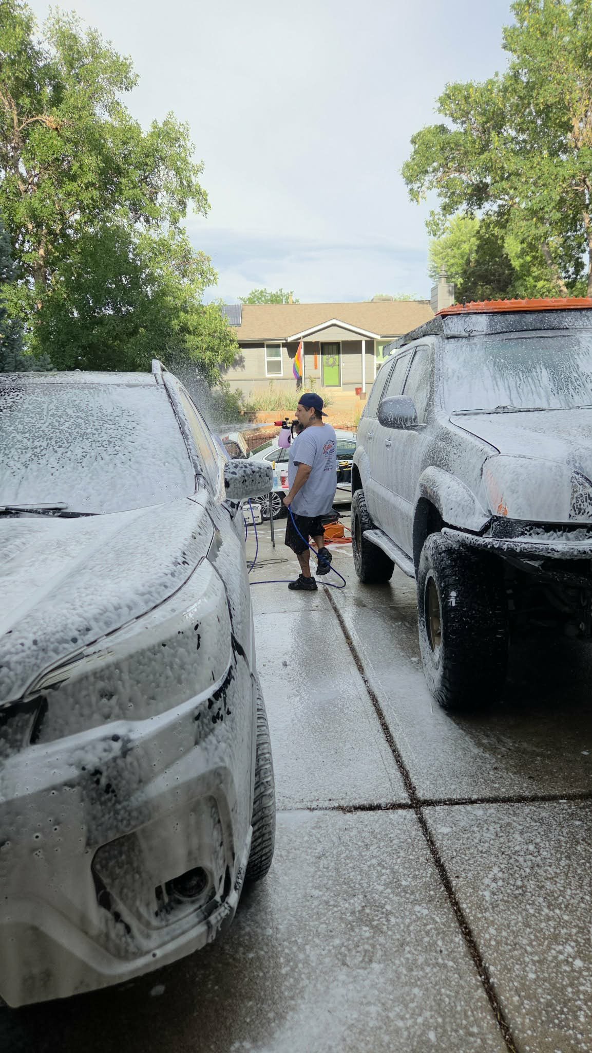 Person pressure-washing two foam-covered vehicles in a residential driveway