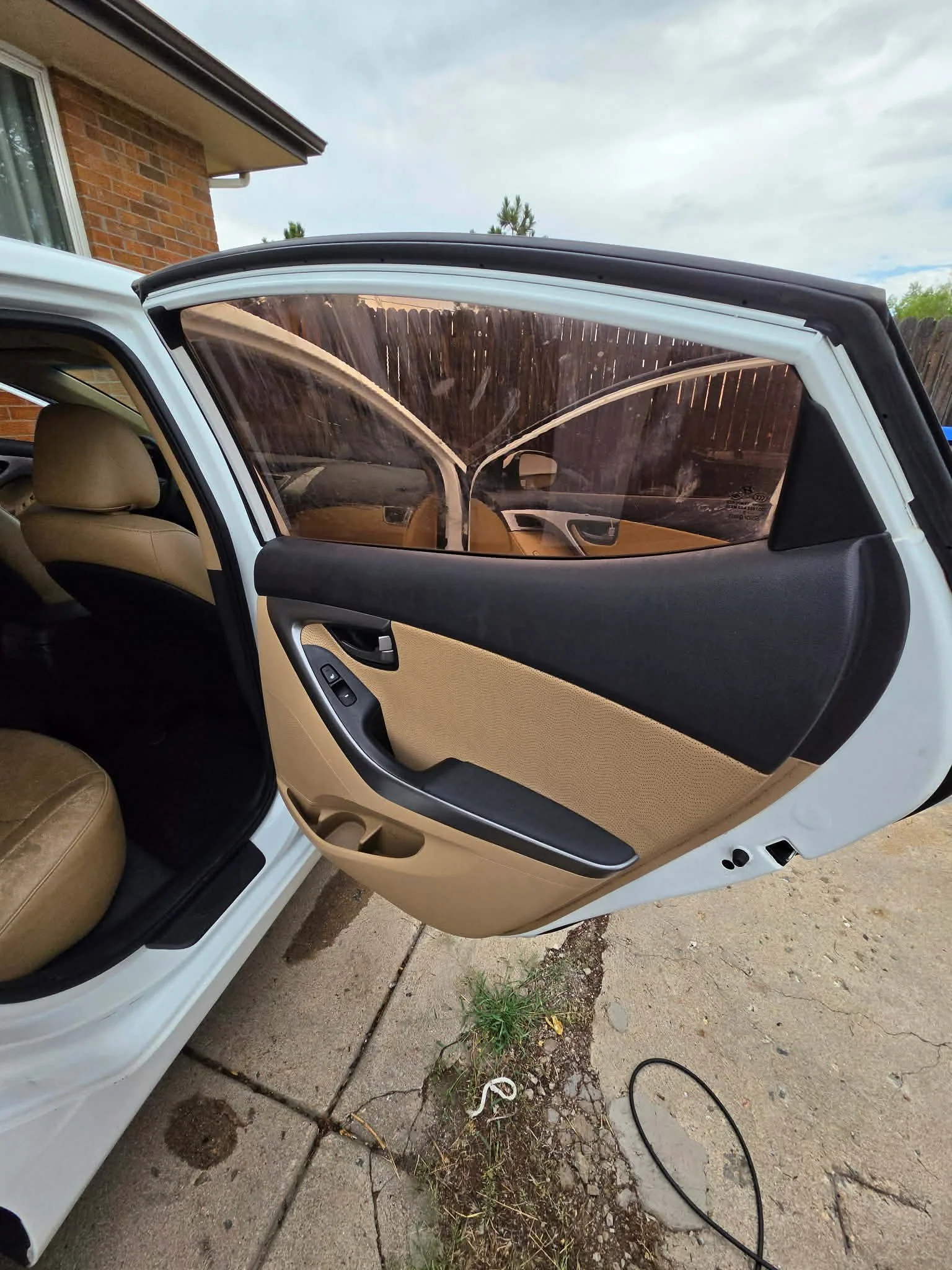 Open white car door with a tan and black interior, power window controls, and damaged side window glass.