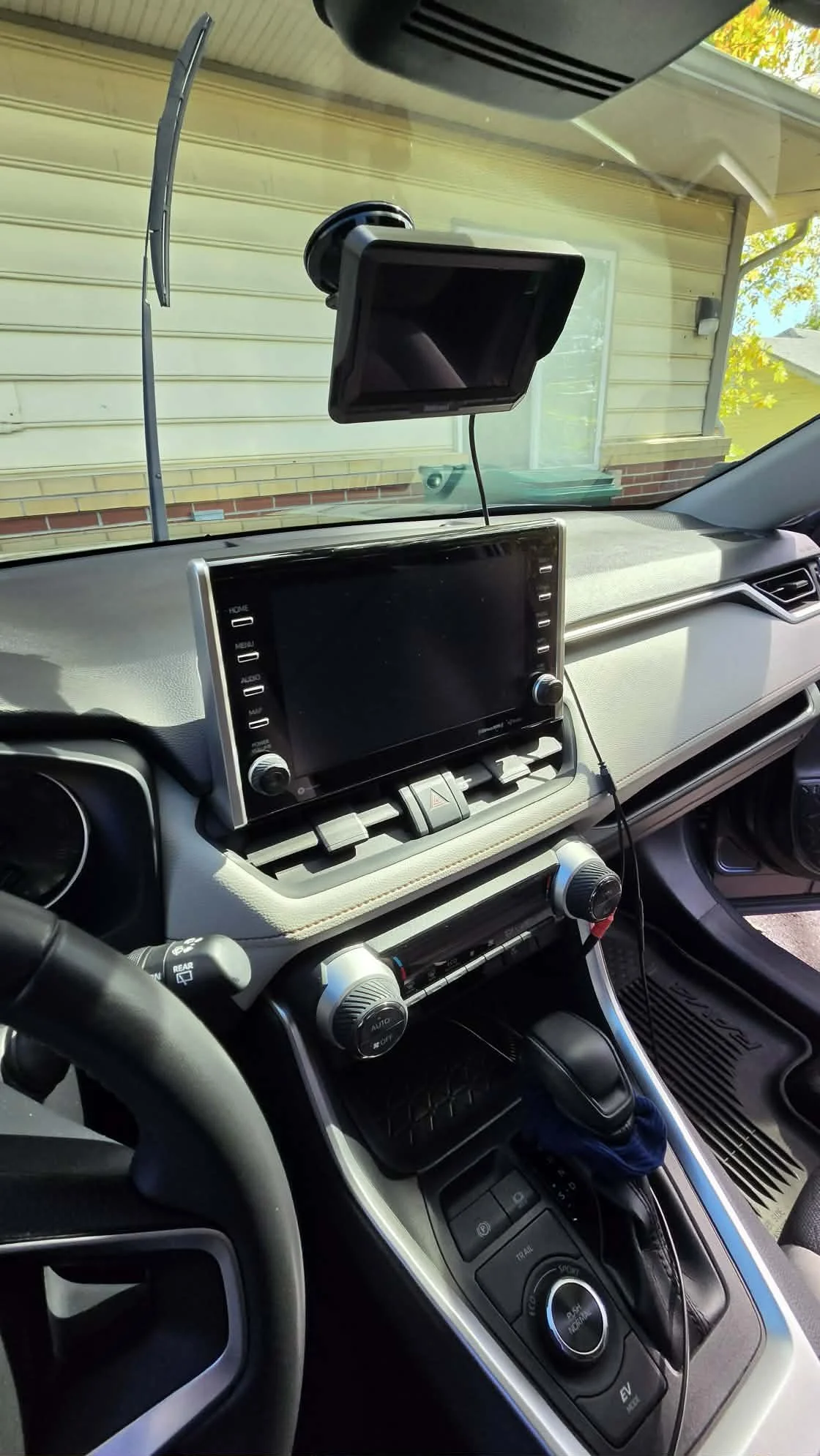 Car interior showing the dashboard, touchscreen infotainment system, climate controls, gear selector, and windshield-mounted display.
