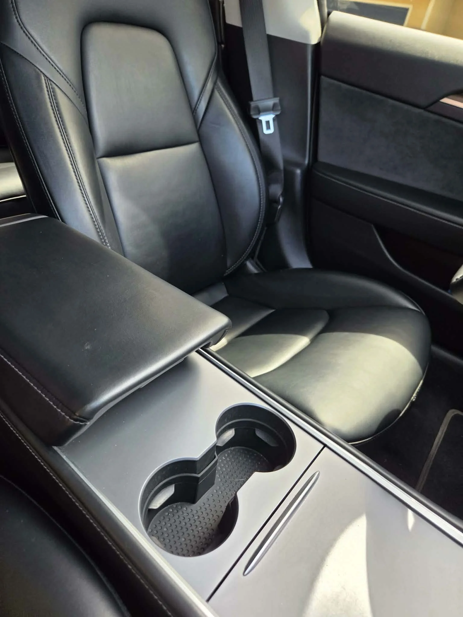 Black leather car interior with passenger seat, seat belt, center armrest, and dual cup holders.