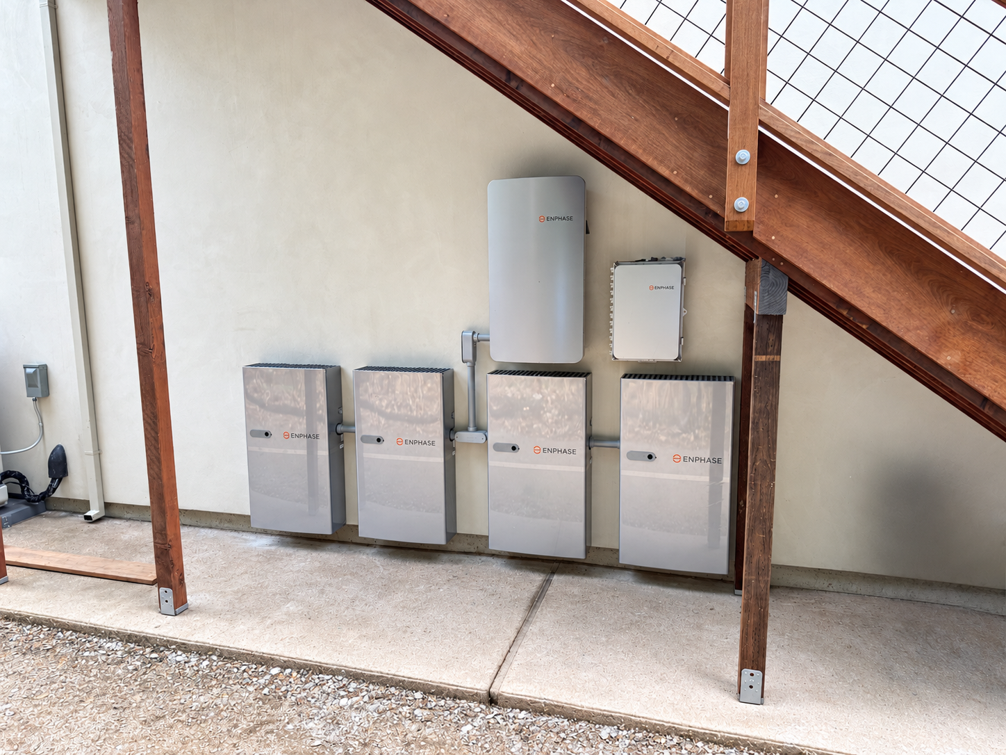 Enphase solar energy storage system with four wall-mounted batteries and control equipment beneath a wooden roof structure