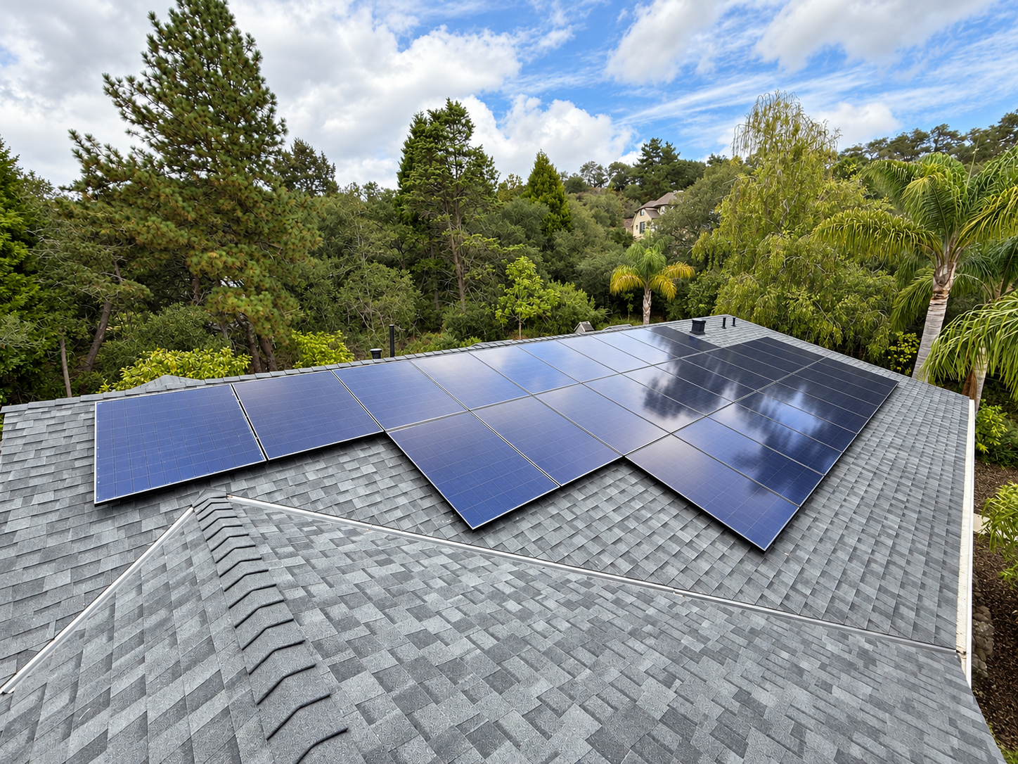 Arrow Energy solar panels on a gray shingle roof surrounded by trees beneath a partly cloudy blue sky.