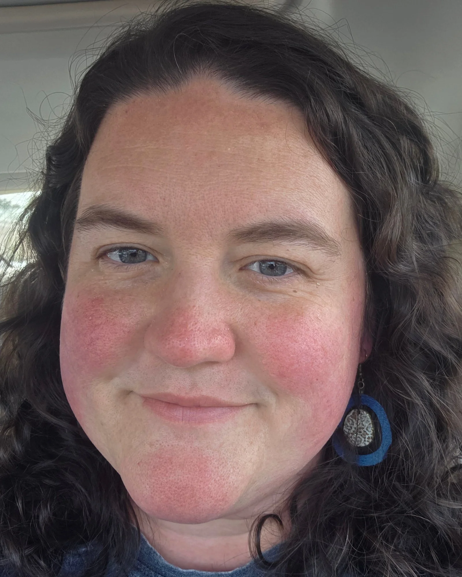 Close-up portrait of a woman with dark curly hair, blue-gray eyes, and earrings
