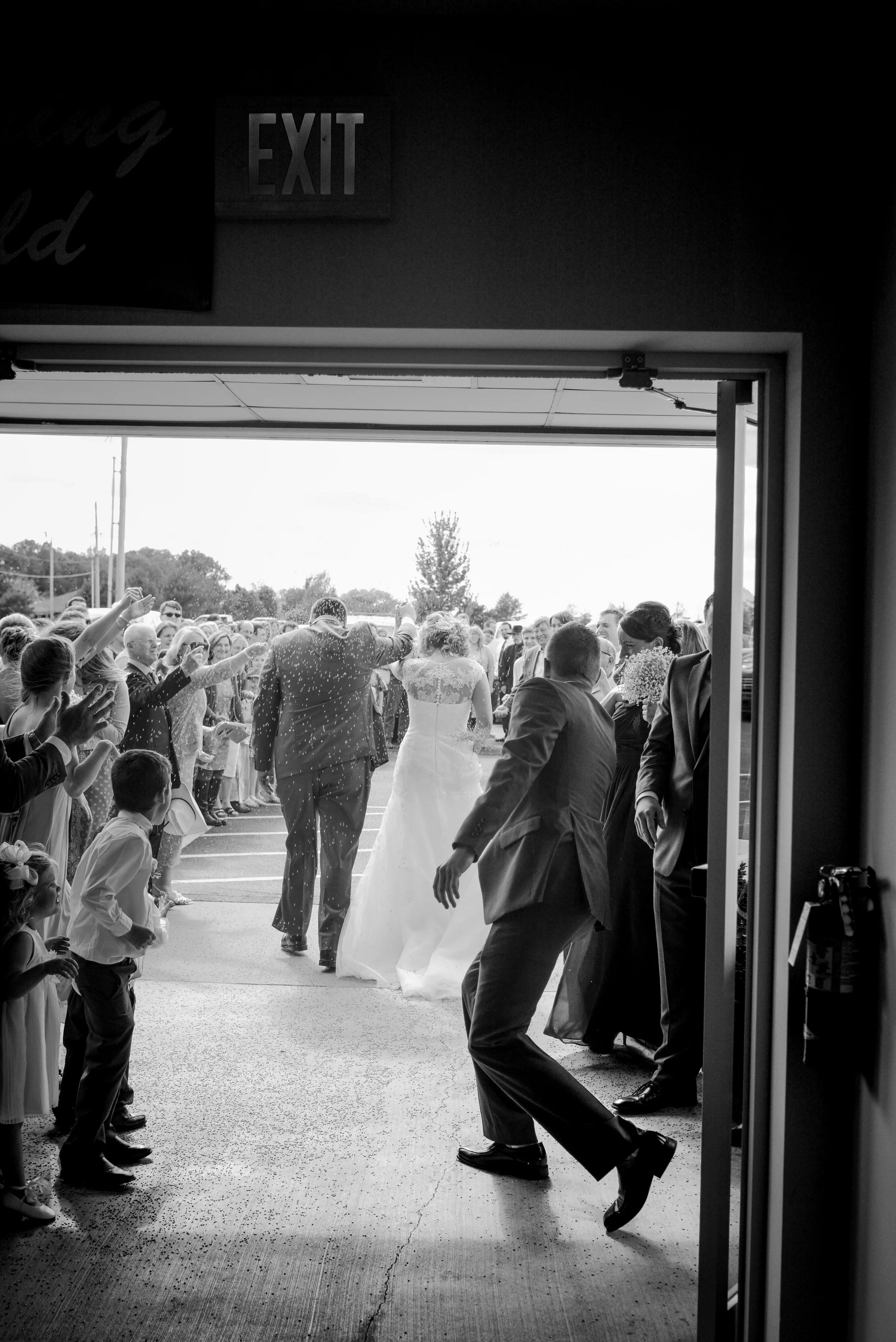 People gathered outside a building with an open door, wedding guests and bride and groom entering, in black and white photo.