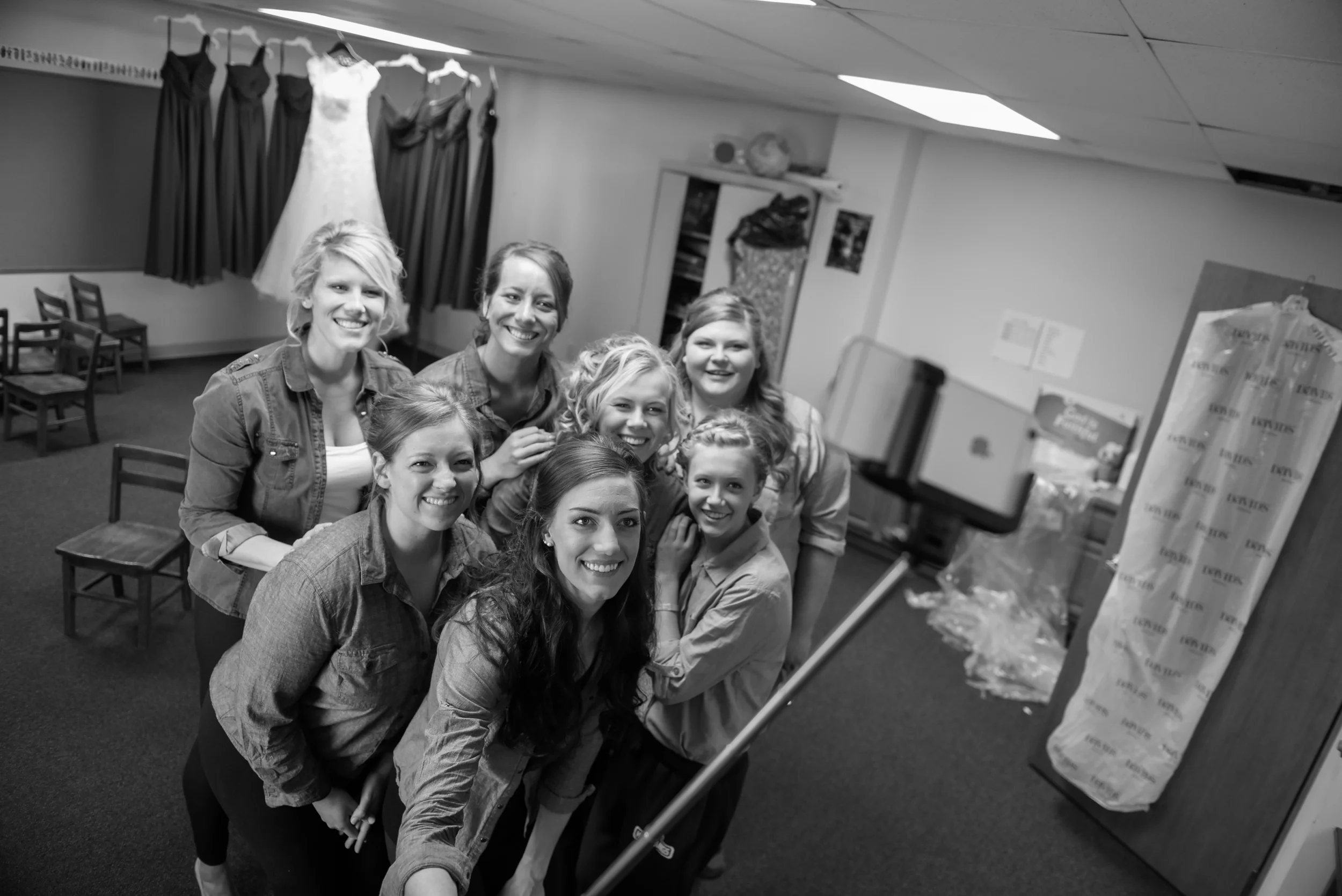 Group of women taking a selfie in a room with dresses hanging on the wall behind them.