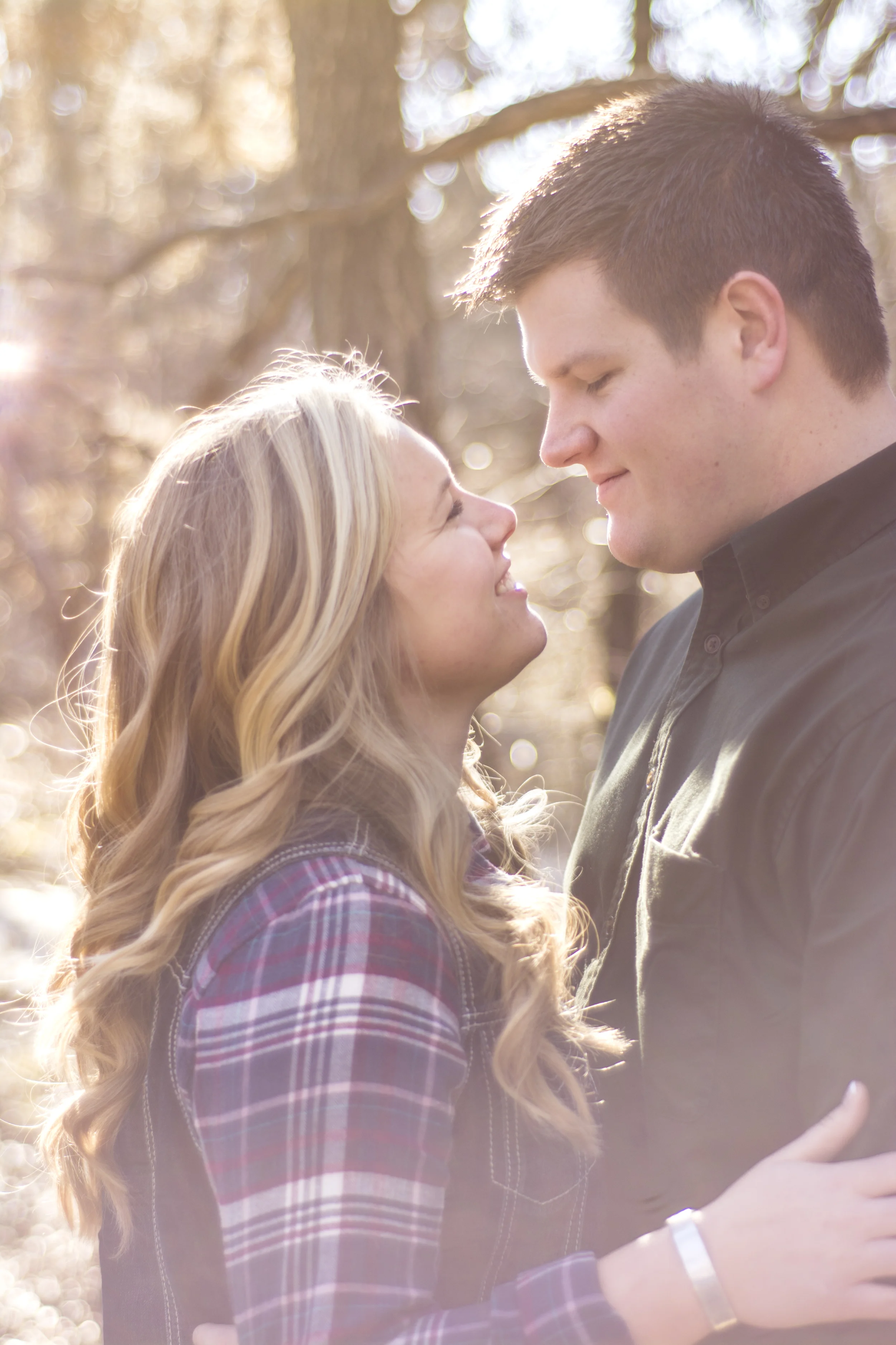 A couple standing close together outdoors, gazing into each other's eyes, with warm backlighting creating a romantic atmosphere.