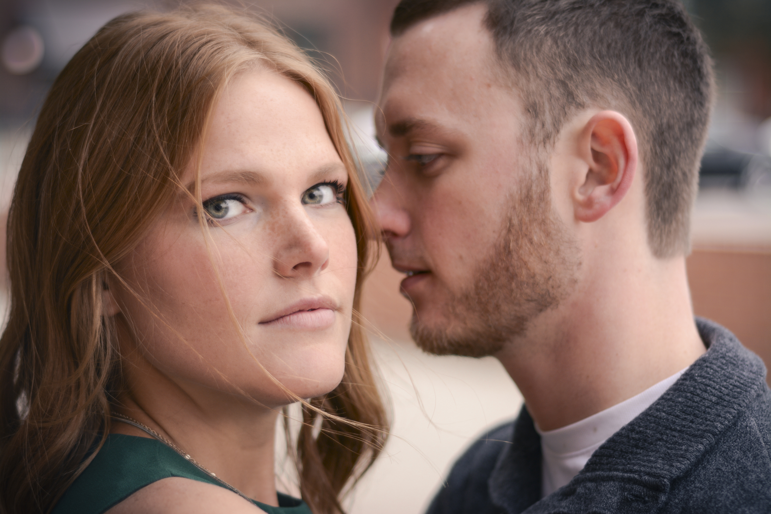 A young woman with red hair and blue eyes looking at a young man with short dark hair and a beard, who is leaning close to her face.