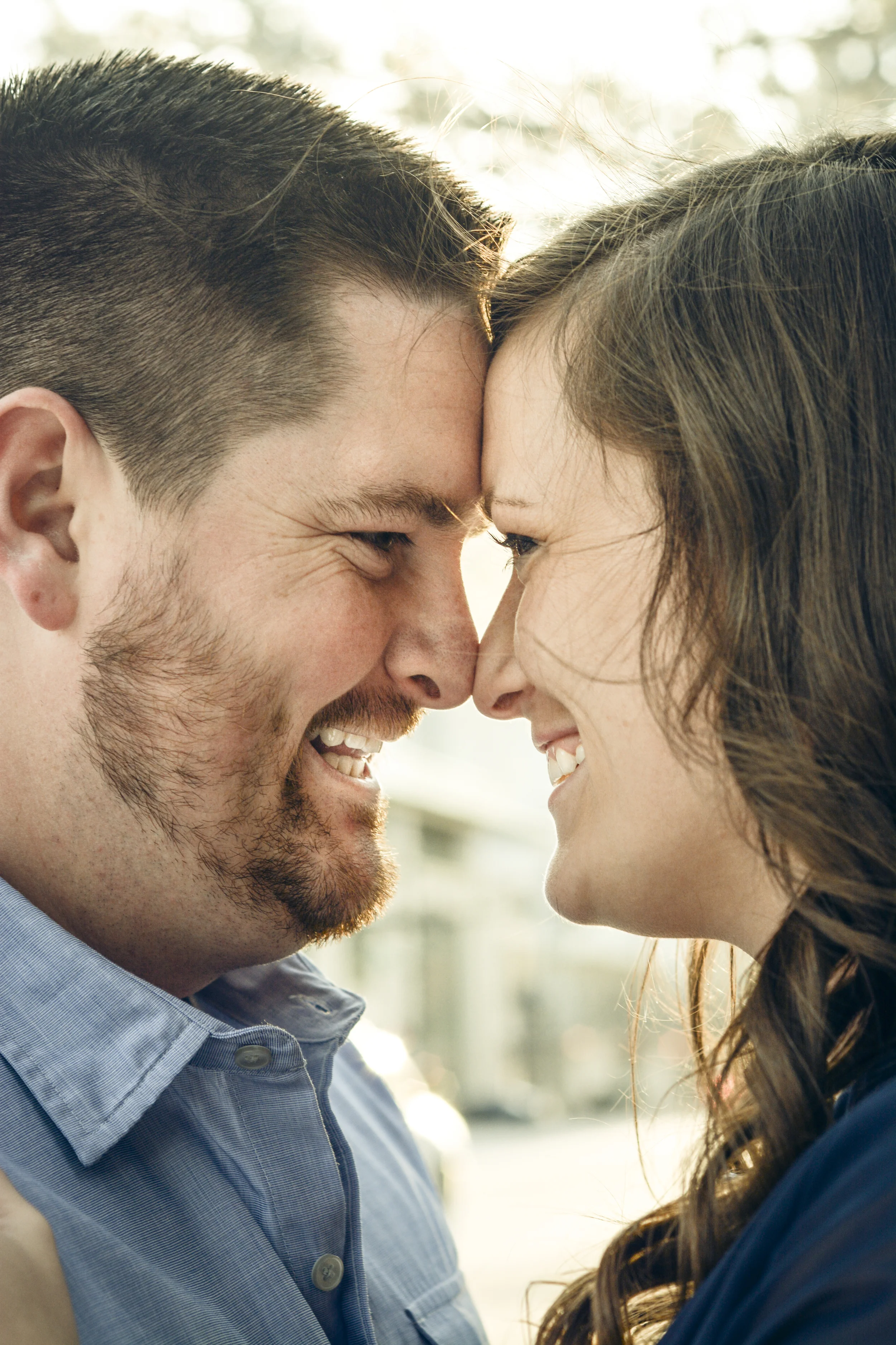 A couple touching foreheads closely smiling with eyes closed in an outdoor setting during daytime.