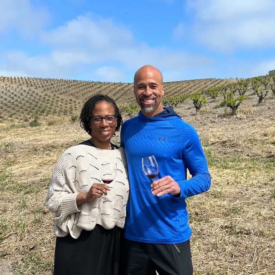 a man and woman standing in a field with wine glasses