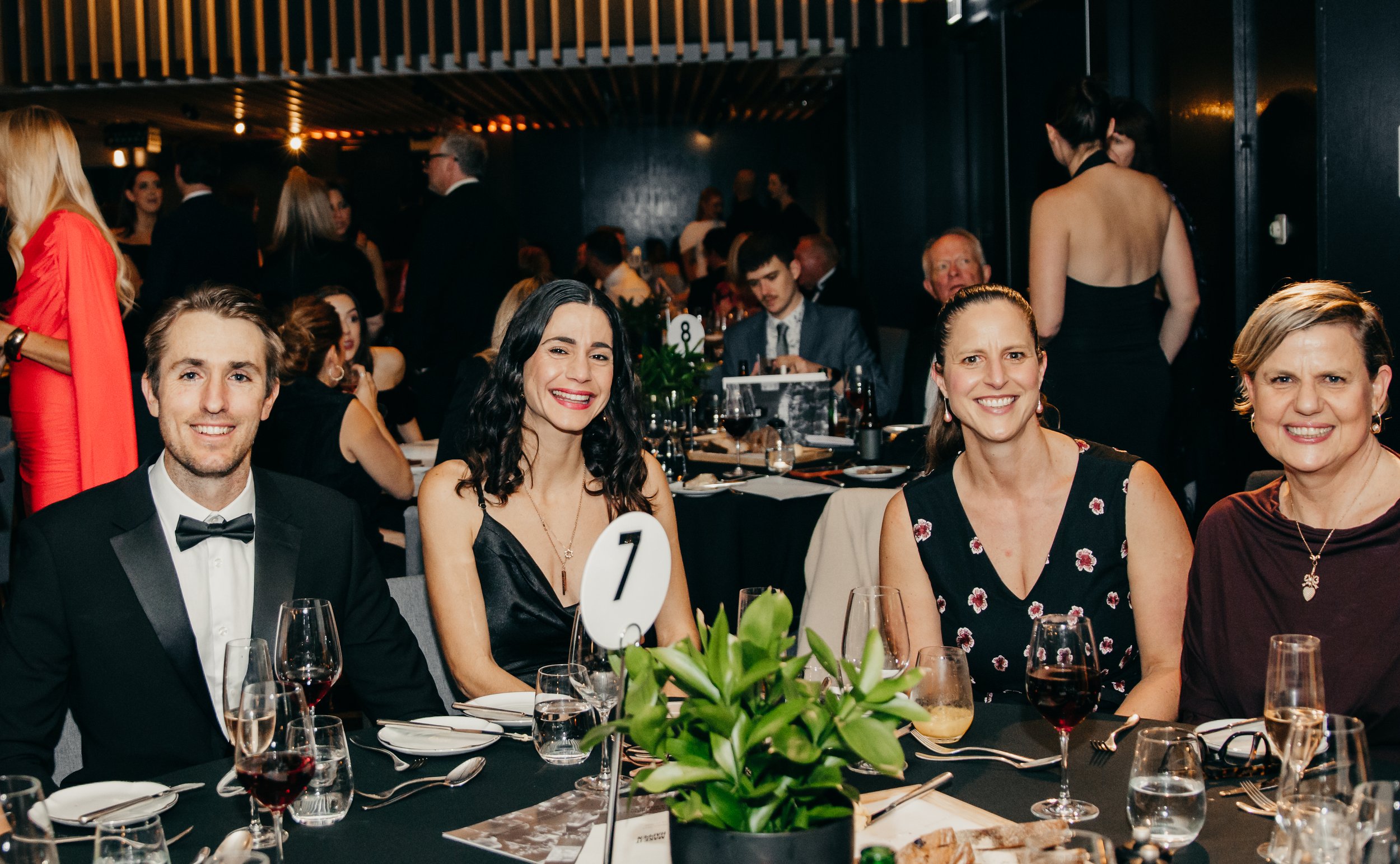 Guests smiling at a formal dinner reception with place settings, wine glasses, and floral centerpieces