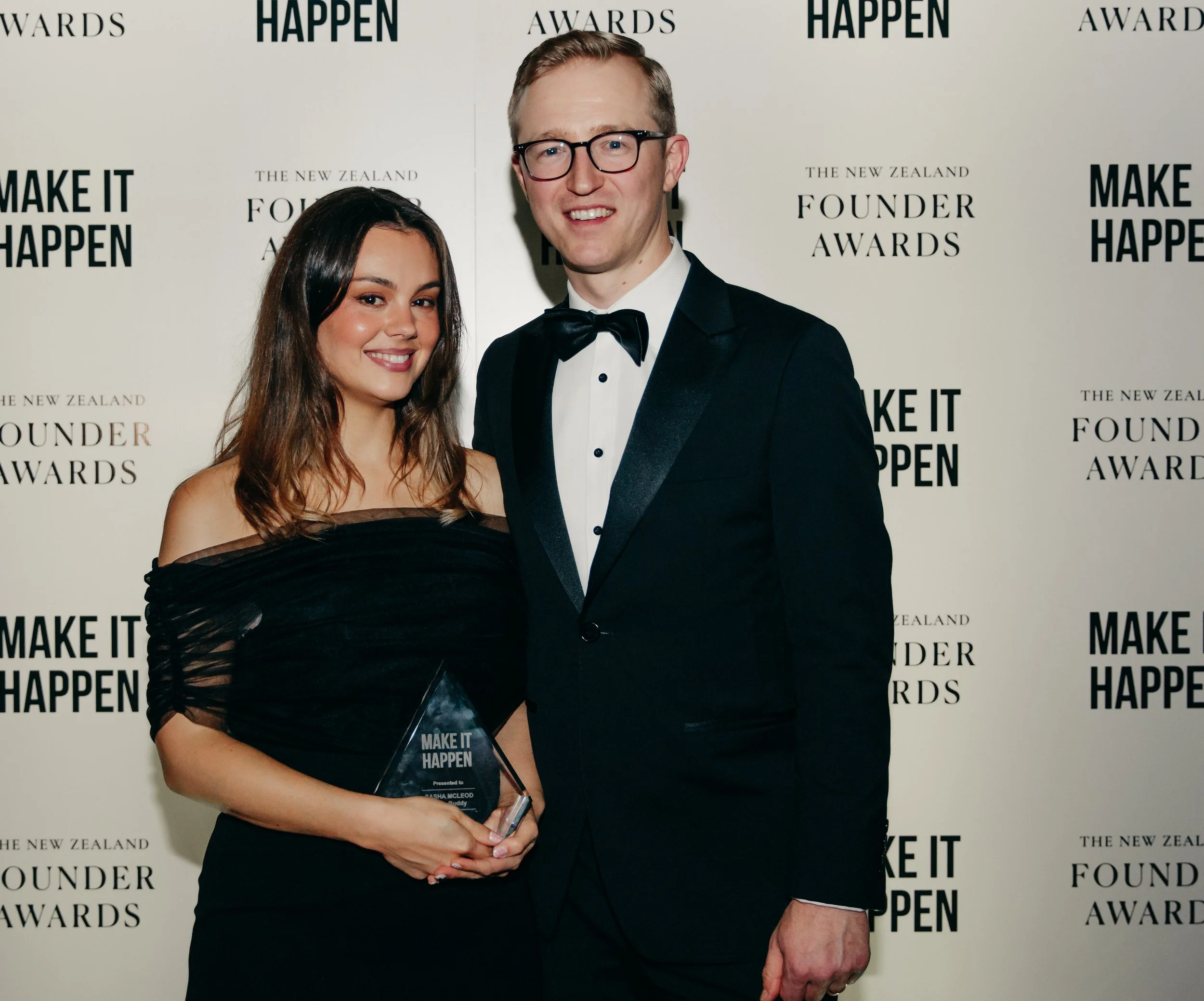 Smiling woman holding a Make It Happen award beside a man in a tuxedo at the New Zealand Founder Awards