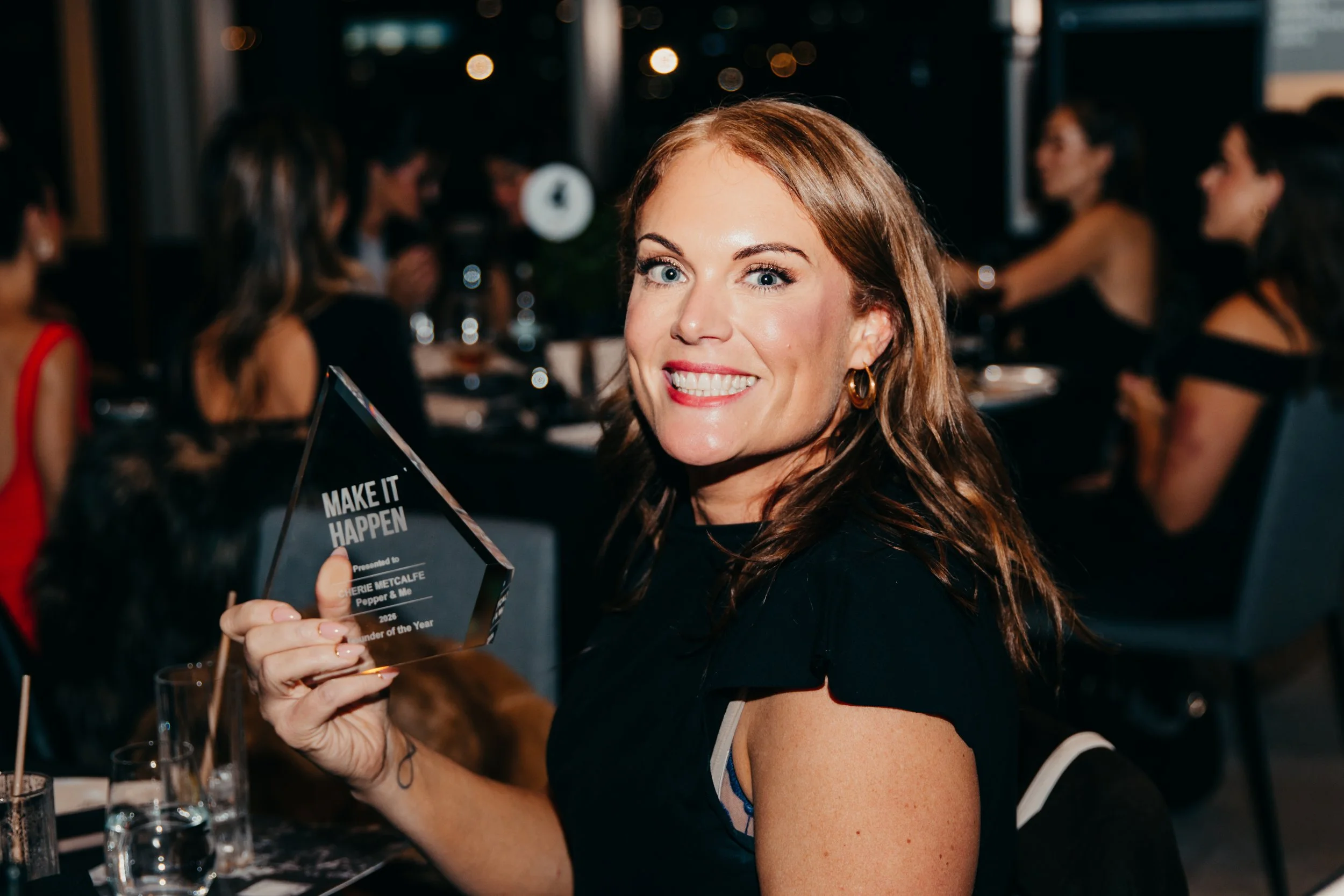 Smiling woman holding a “Make It Happen” award at a nighttime event