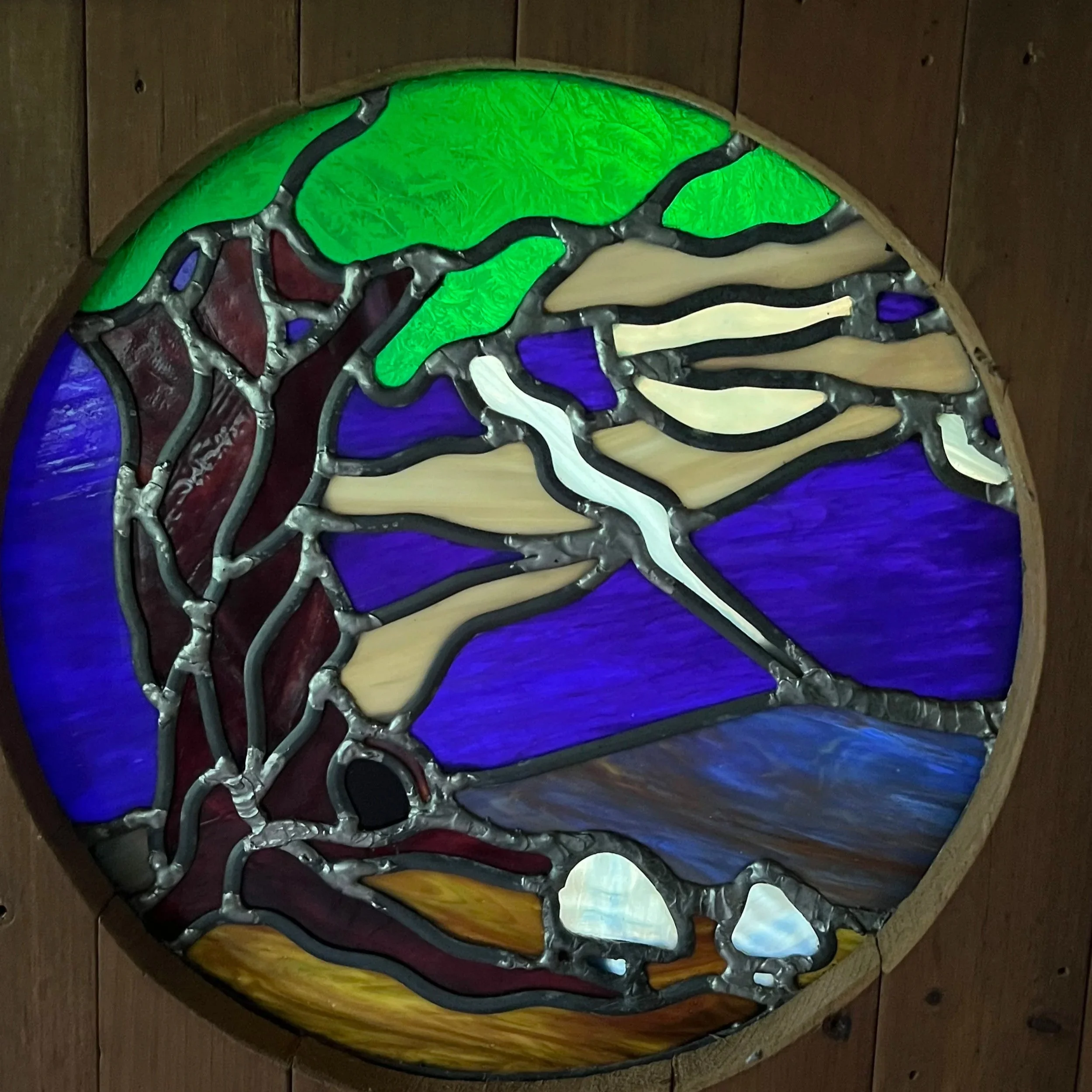 Colorful stained-glass dragonfly with green wings and purple, cream, and blue glass details mounted on a wooden wall