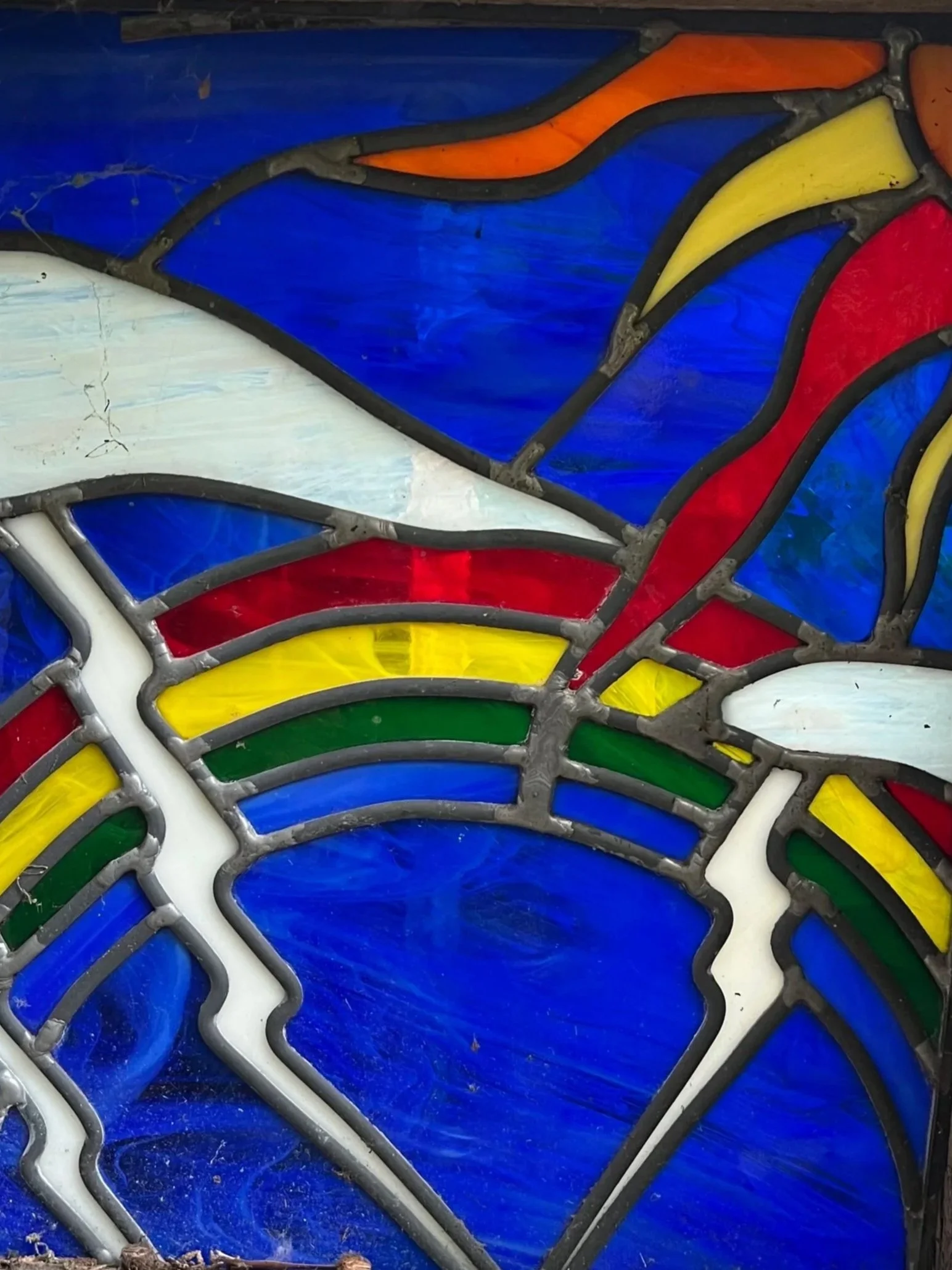 Close-up of colorful stained glass artwork with blue, red, yellow, green, orange, and white glass pieces in dark lead came.