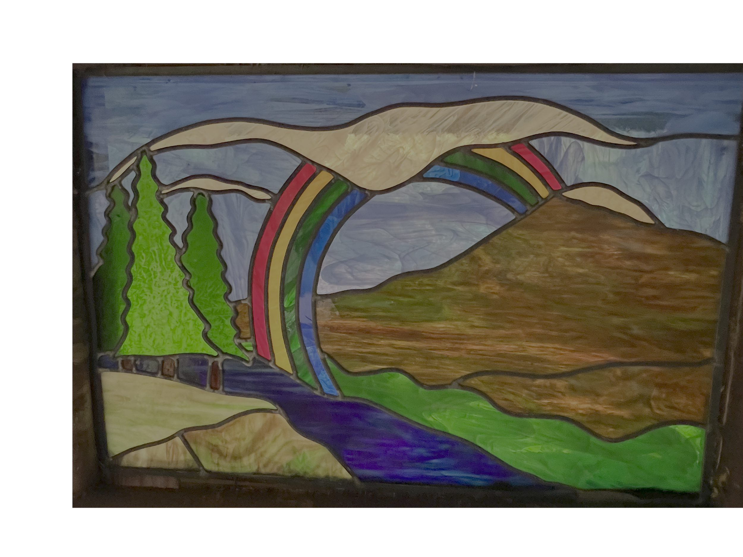 Stained-glass landscape depicting a rainbow over evergreen trees, mountains, a river, and a large brown rock formation