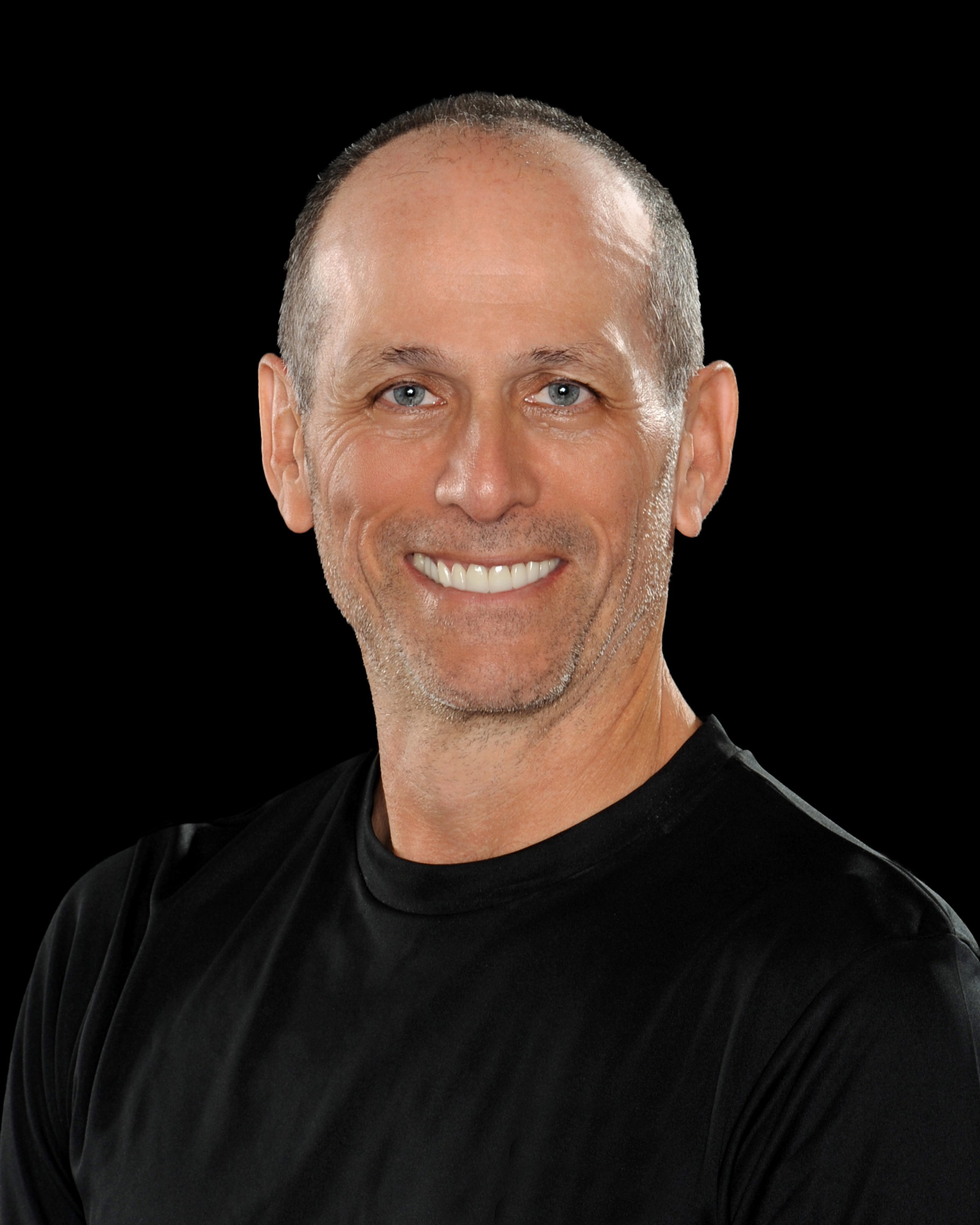 Smiling middle-aged man with short gray hair and stubble wearing a black shirt against a black background