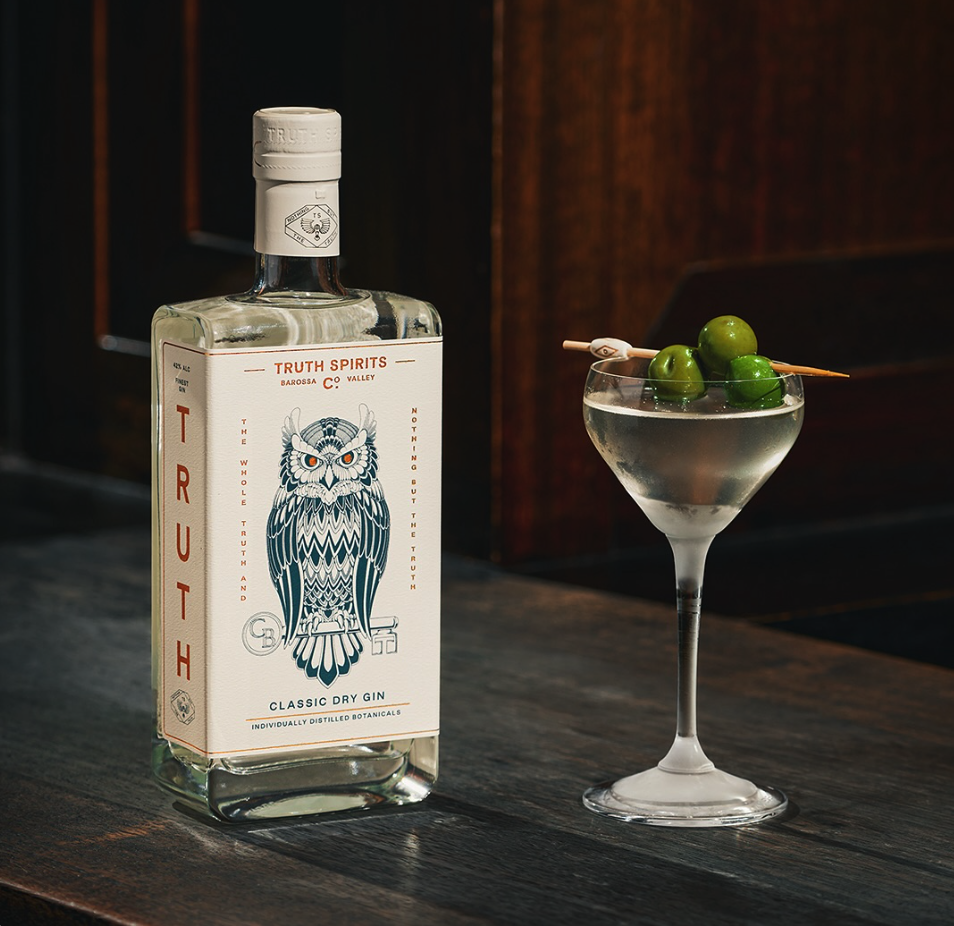Truth Spirits Classic Dry Gin bottle beside a coupe cocktail garnished with green olives on a wooden bar