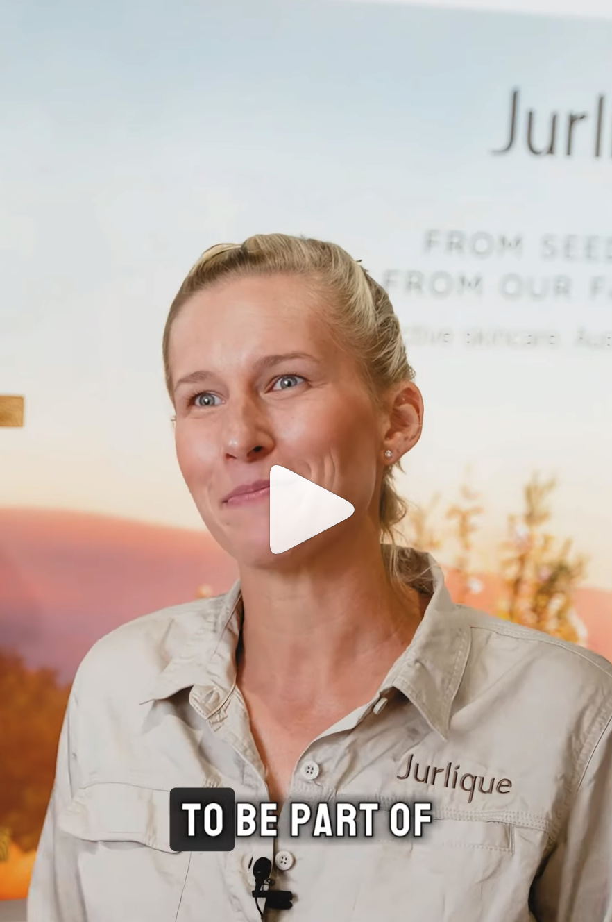 Blonde woman in a Jurlique shirt speaking in a promotional video with a play button overlay