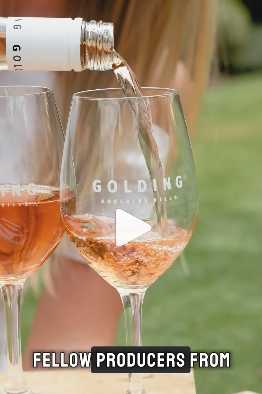 White wine being poured from a Golding Wines bottle into a branded wine glass beside a filled glass