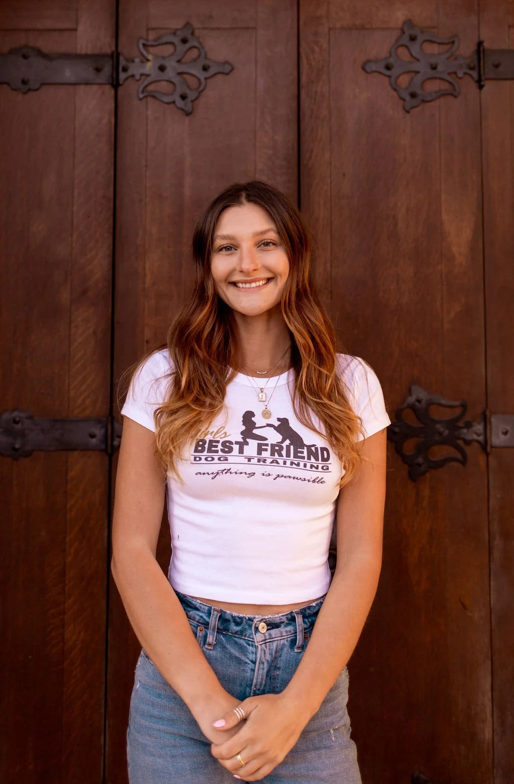 Smiling woman in a white Best Friend Dog Training T-shirt standing in front of a wooden door