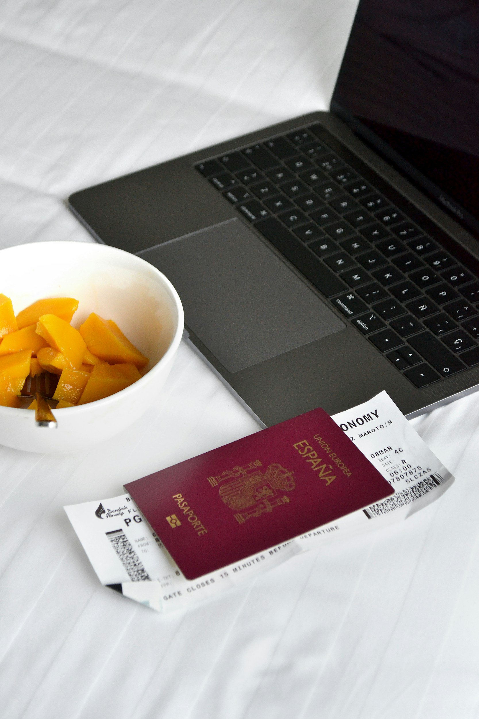 Passport and travel documents arranged on a bed beside an open laptop.
