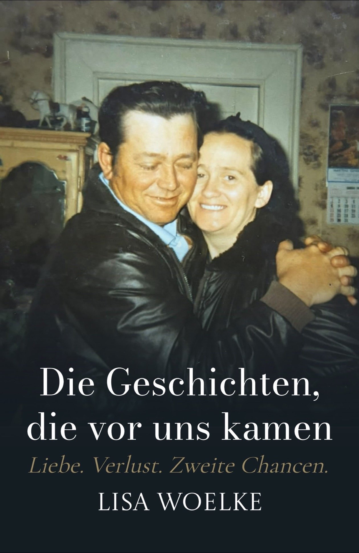 Cover of a book titled 'Die Geschichten, die vor uns kamen' by Lisa Woelke, featuring a photograph of a man and woman hugging and smiling, with a background of a rustic room with wooden furniture and a calendar on the wall.