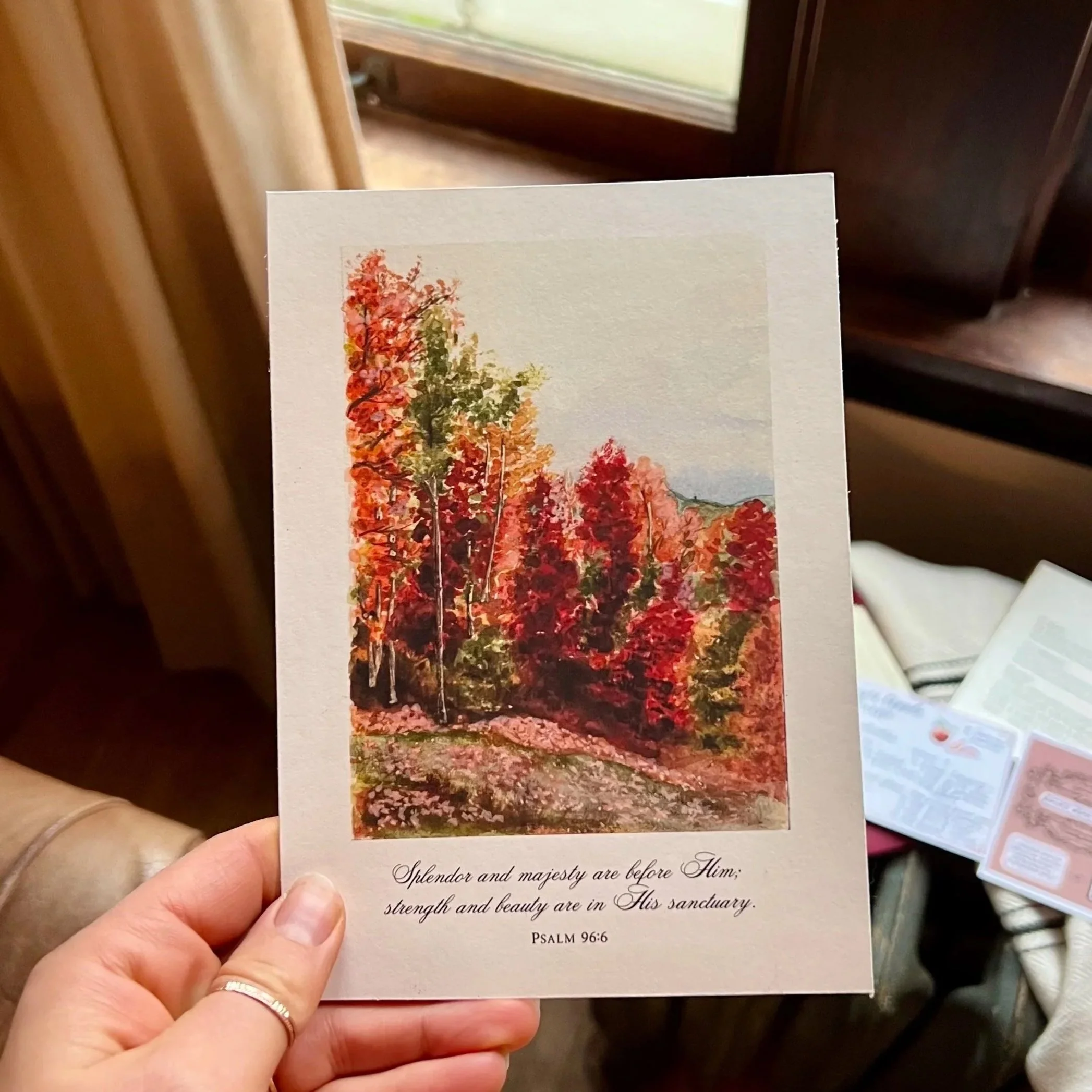 Hand holding a religious card featuring colorful autumn trees and Psalm 96:6
