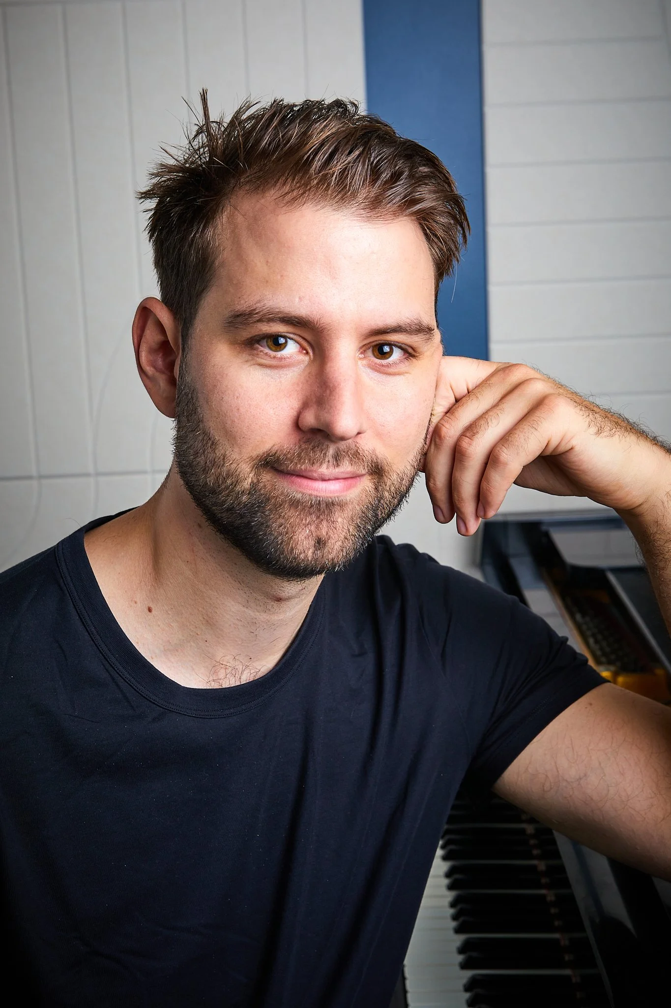 Bearded man in a black shirt posing beside a piano keyboard