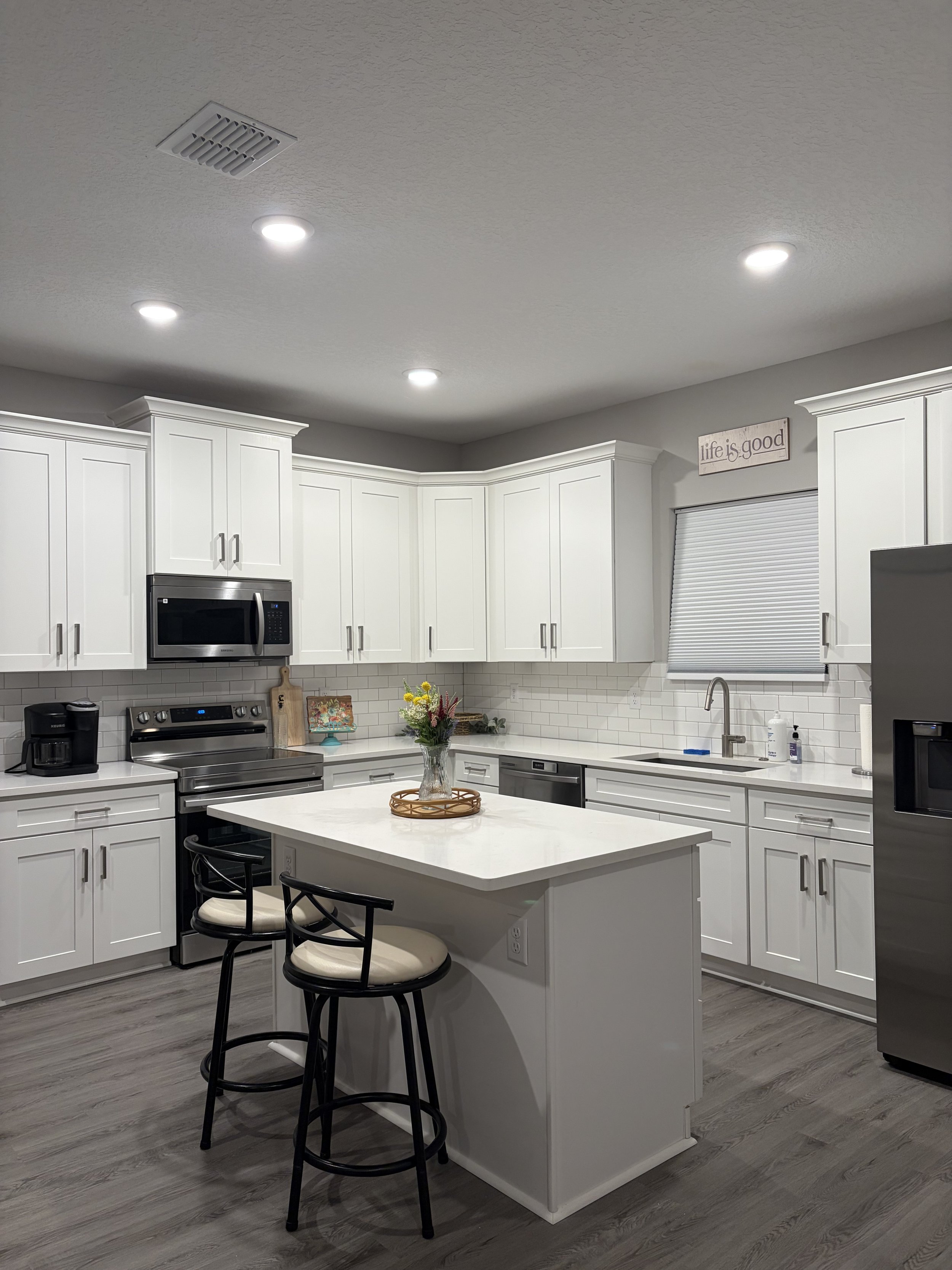 Bright modern kitchen with white cabinets, stainless steel appliances, subway tile backsplash, large island, bar stools, and recessed lighting