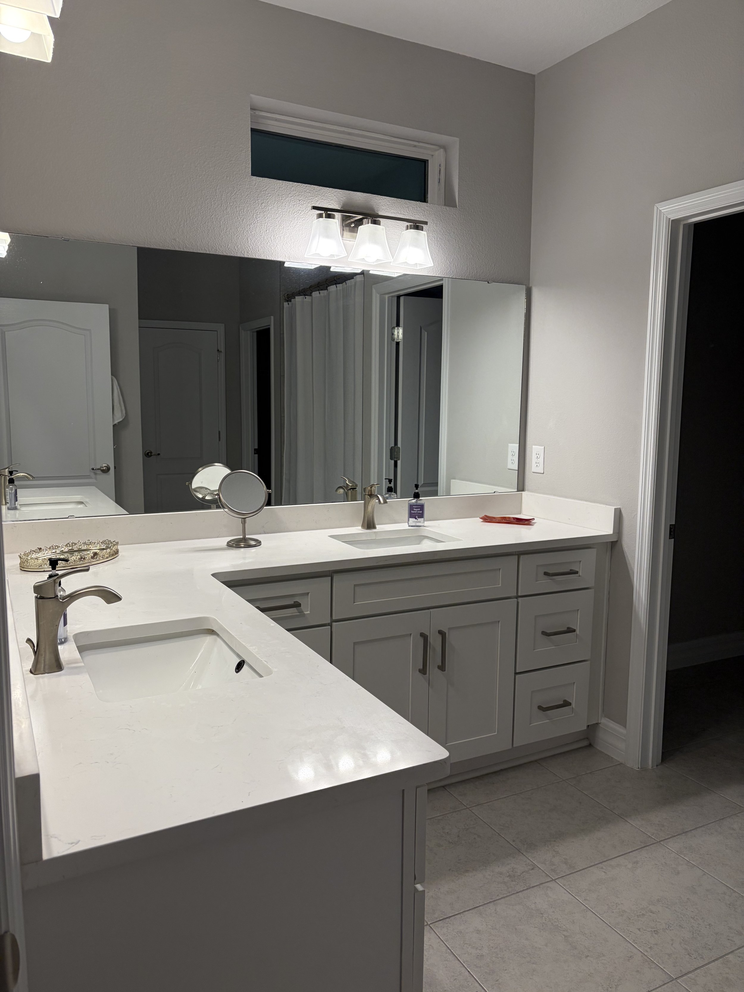 Modern gray bathroom vanity with double sinks, white countertop, large mirror, and three-light fixture
