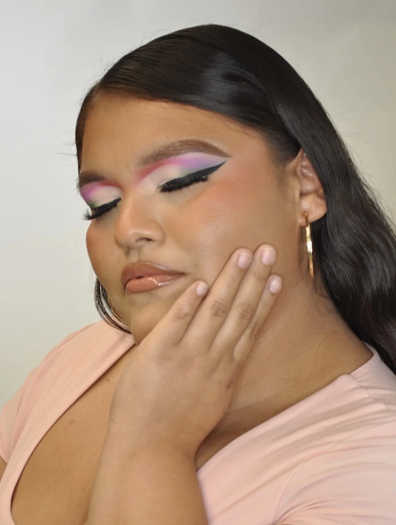 Close-up portrait of a woman showcasing pink and lavender eyeshadow, dramatic winged eyeliner, and glossy nude lips.