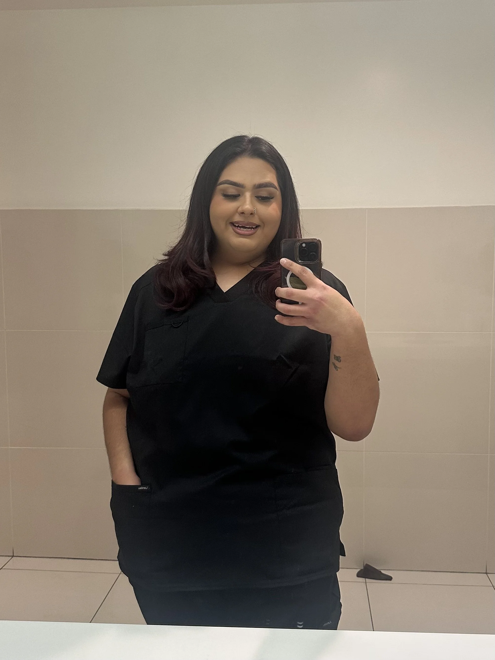 Person in black medical scrubs taking a mirror selfie with a smartphone